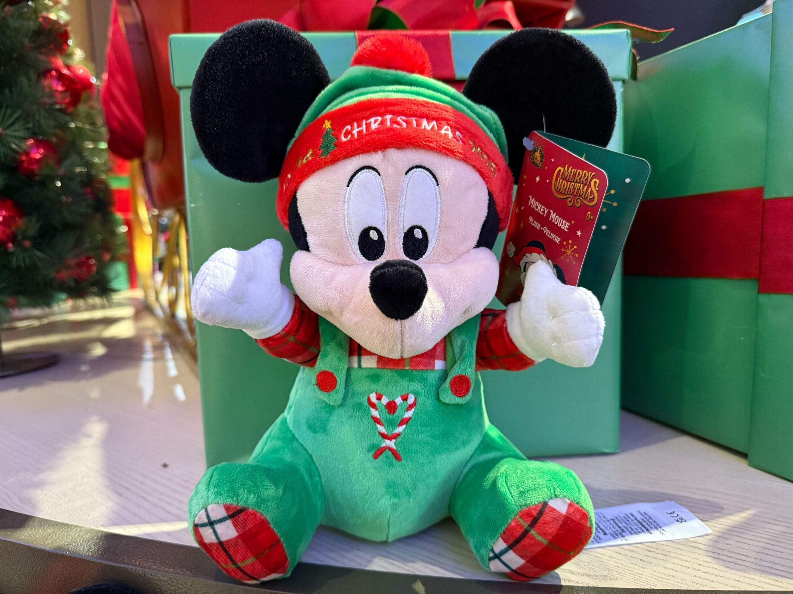 Plush Mickey Mouse doll in festive green holiday outfit, classic Christmas merch from Disneyland Resort, home of Sleeping Beauty Castle.