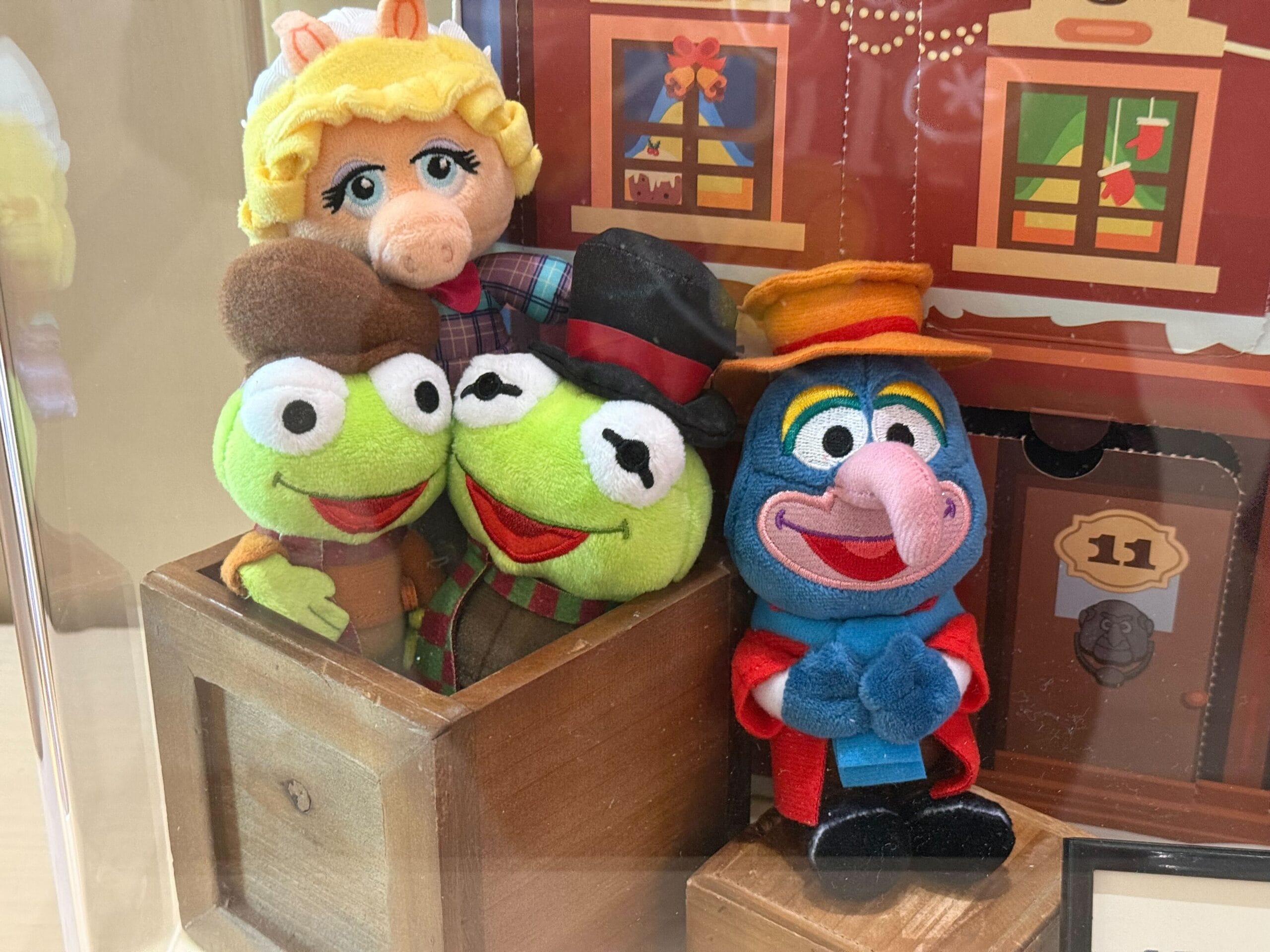 Four Muppet plush toys, including Kermit and Miss Piggy, sit by a Christmas box—classic Disneyland Resort holiday merchandise.