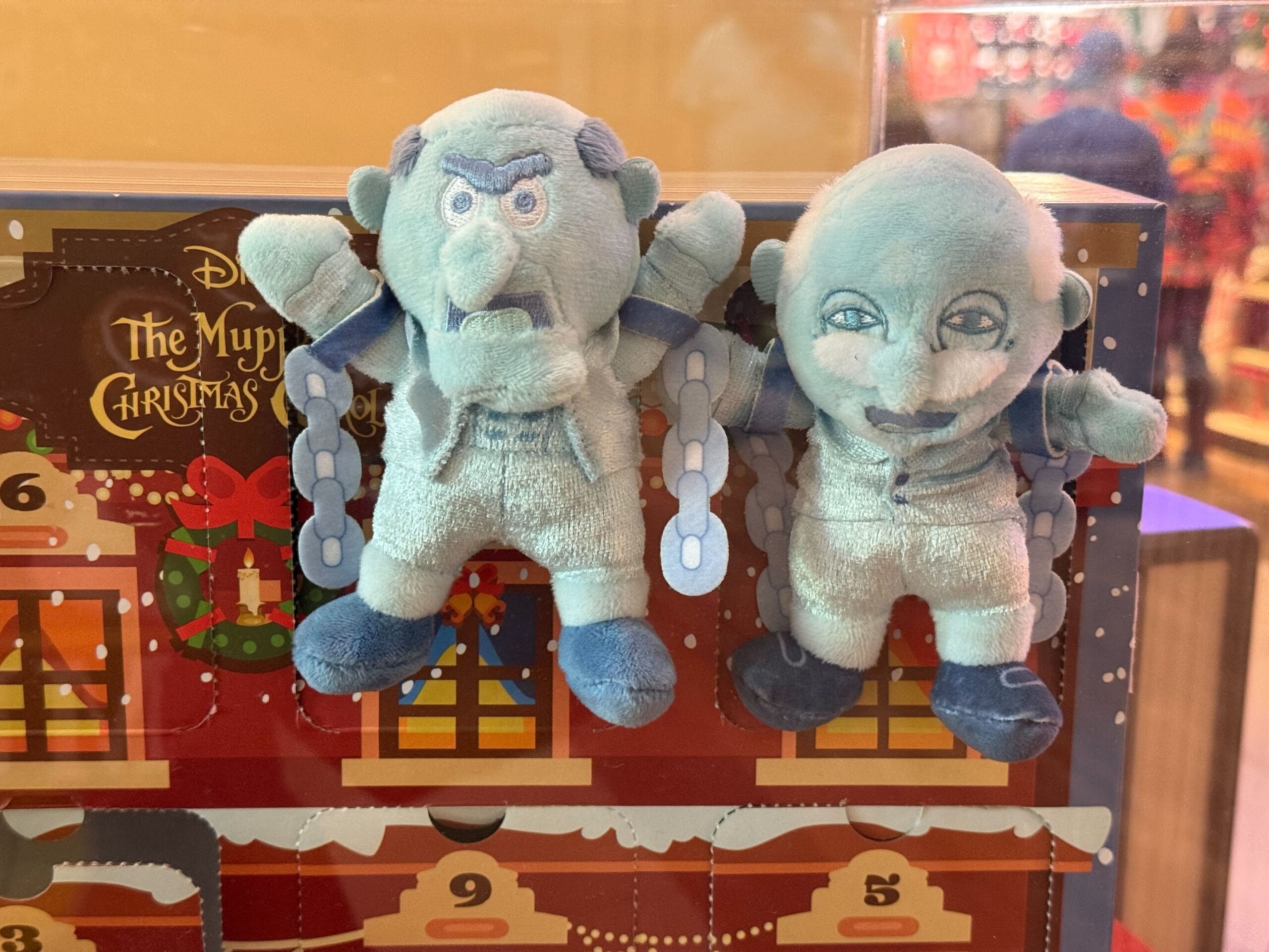 Two blue Muppet plush toys with chains atop festive Christmas merch, featured as new arrivals at Disneyland Resort gift shops.