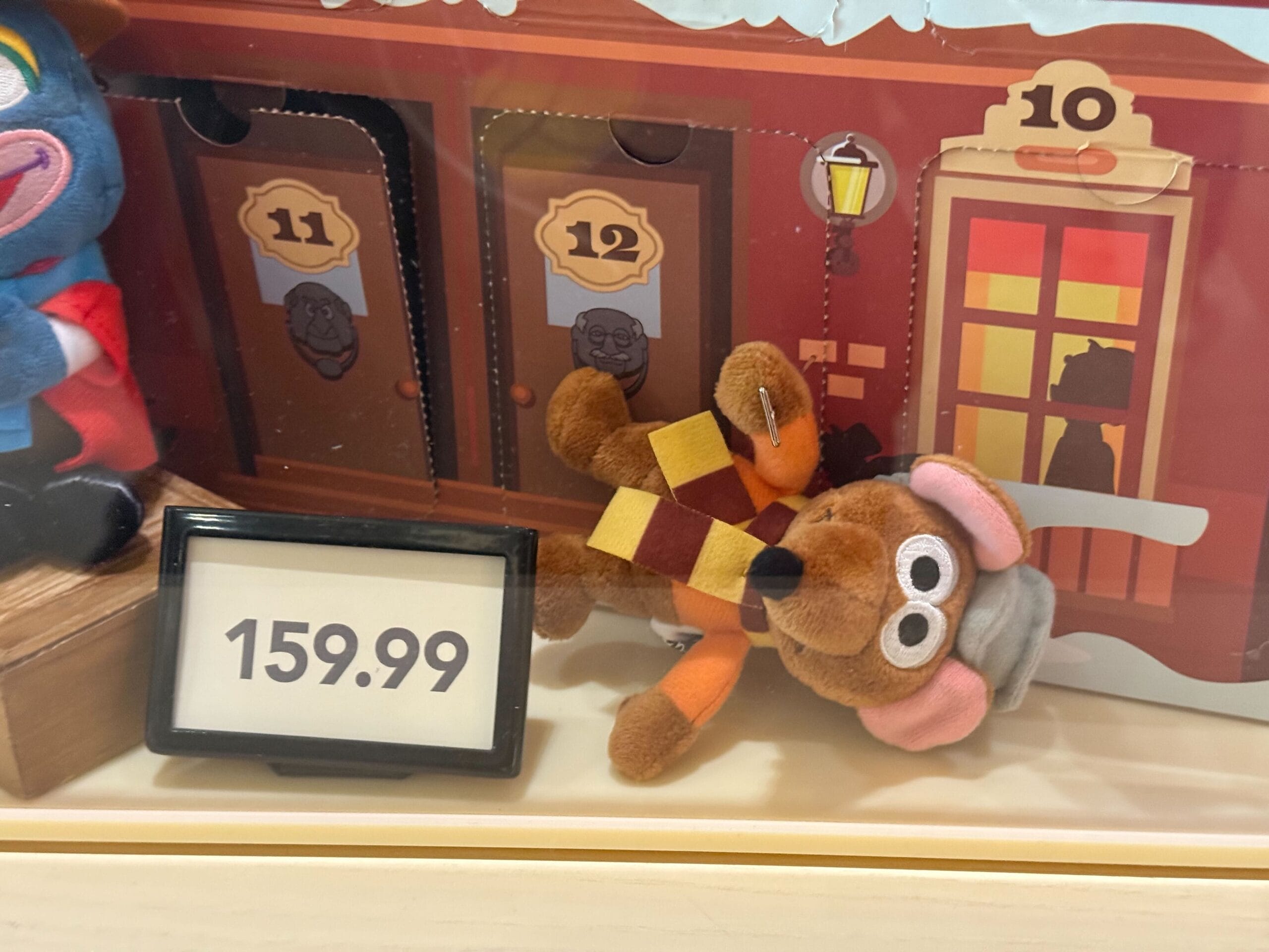Disneyland Resort Christmas plush with glasses and scarf, sits near toy train set—merchandise priced at $159.99.