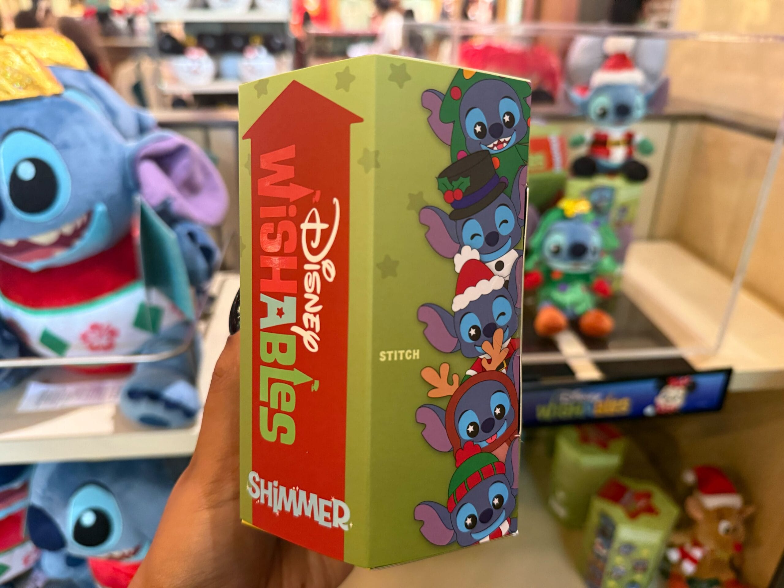 A hand holds a Disney Wishables box with Stitch in holiday attire, classic Christmas merch often found at Disney Parks worldwide.