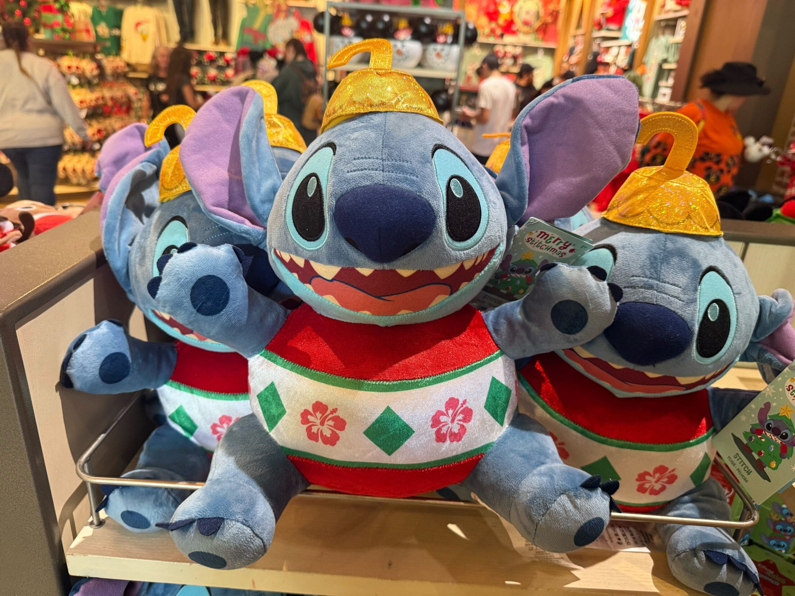 Festive Stitch plush toys in holiday outfits stacked on a Disneyland Resort shelf, part of the exclusive Christmas collection.