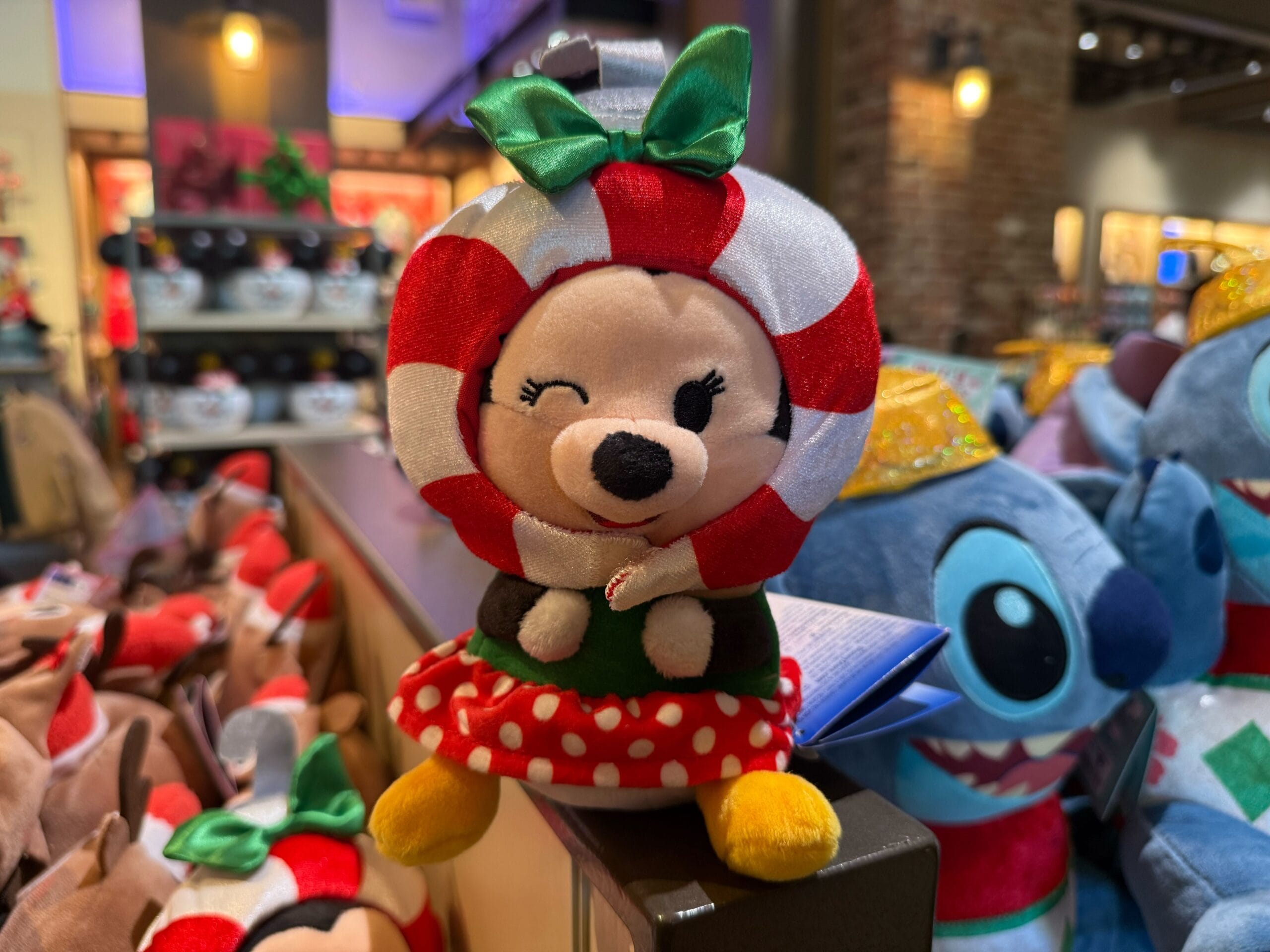 A plush Minnie Mouse dressed as a peppermint candy winks and smiles among festive Christmas merchandise at Disneyland Resort.