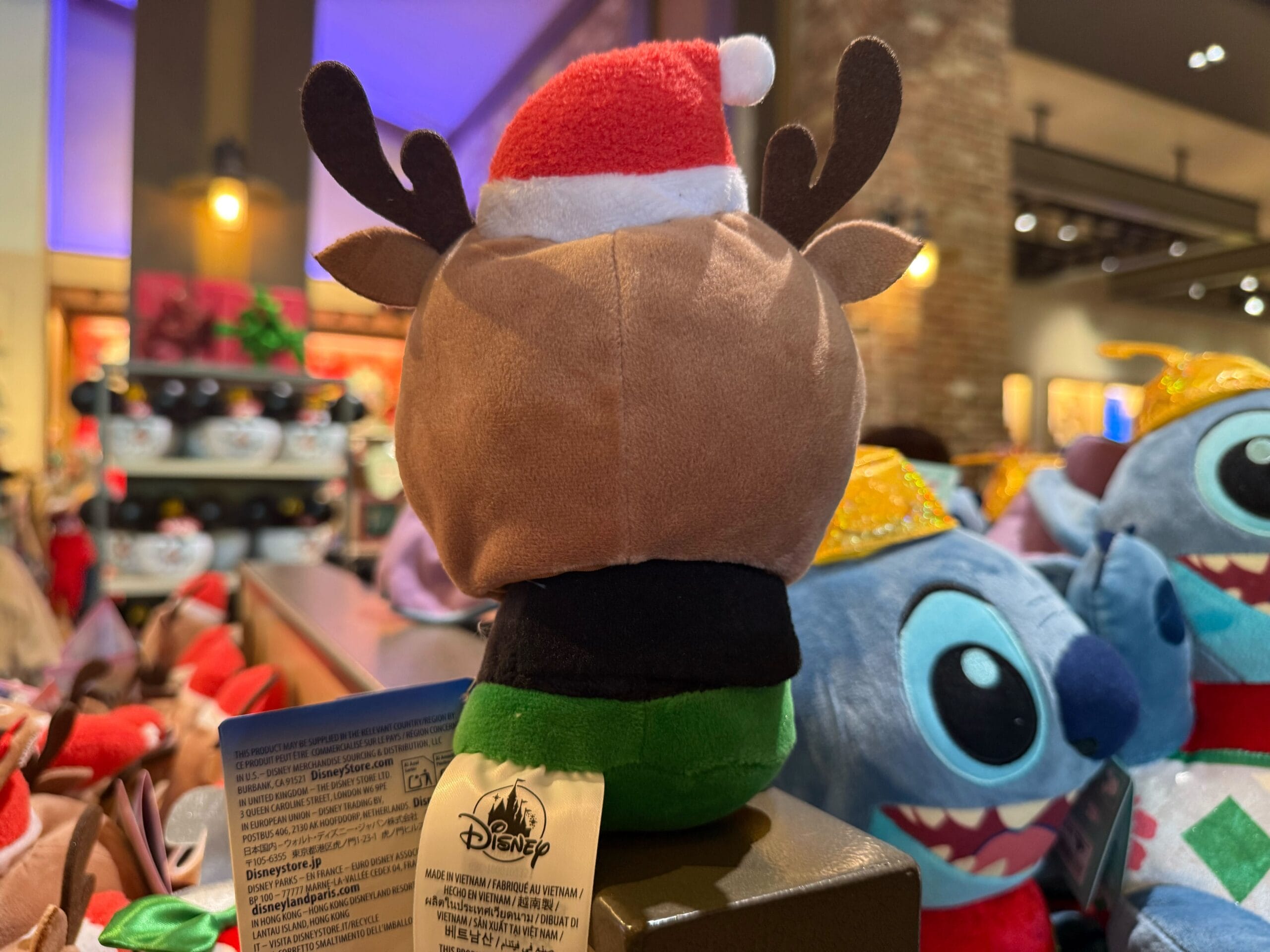 Plush toy with antlers and Santa hat, part of Disneyland Resort holiday merch, surrounded by festive stuffed toys.