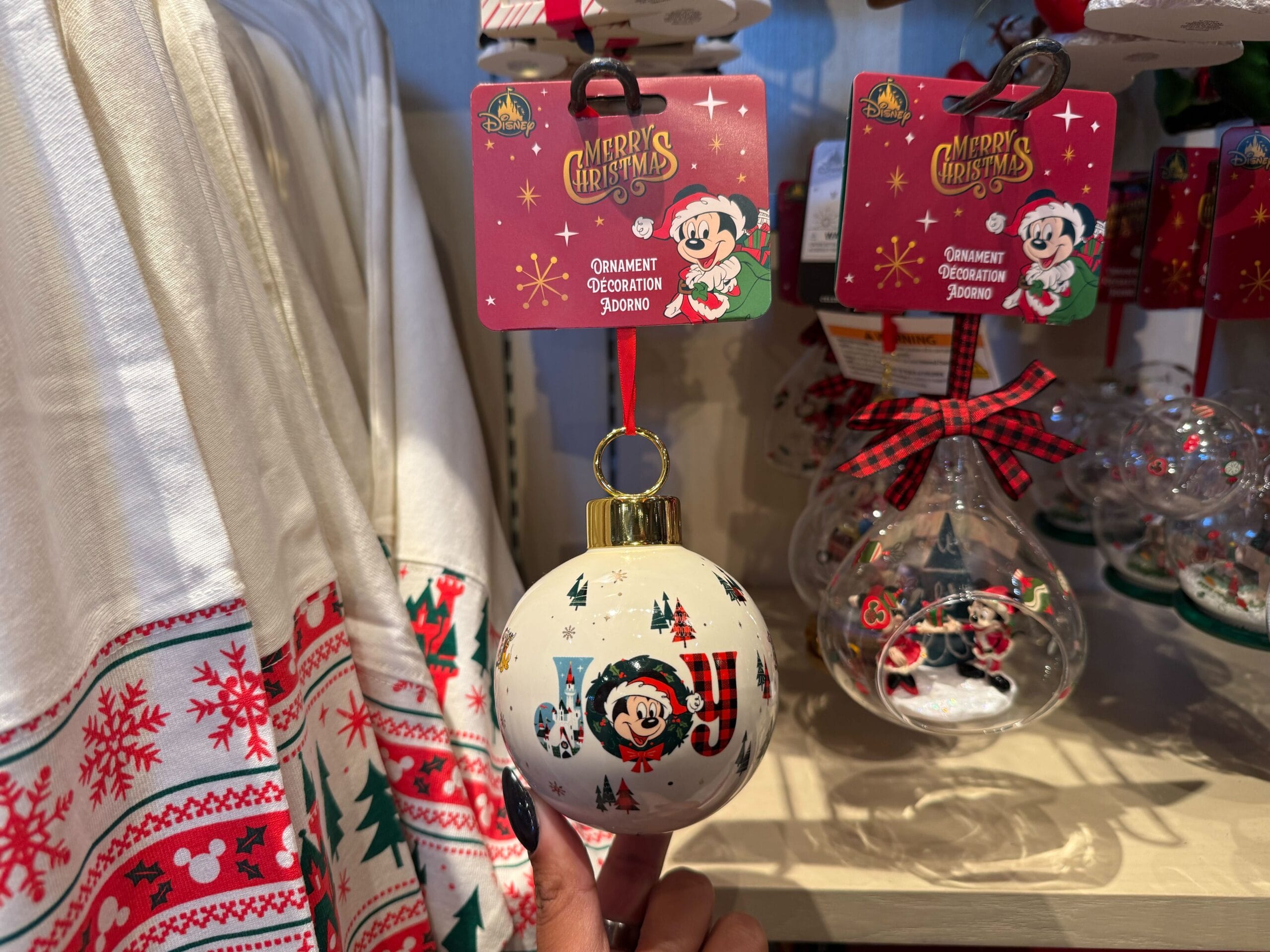 A hand holds a white Christmas ornament from Disneyland Resort, decorated with festive Mickey Mouse, distinct from Disney World's style.
