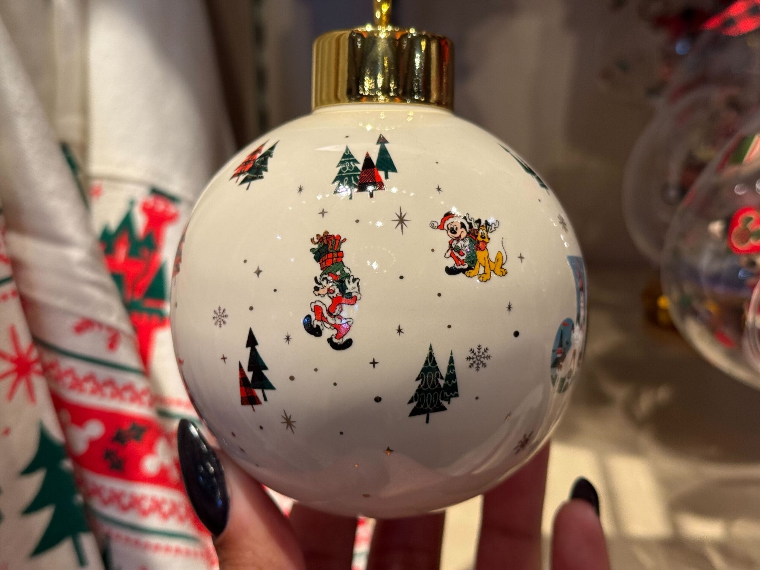Festive white ornament with Mickey, Pluto, trees & snowflakes—Disneyland Resort exclusive, not featuring any park castle design.