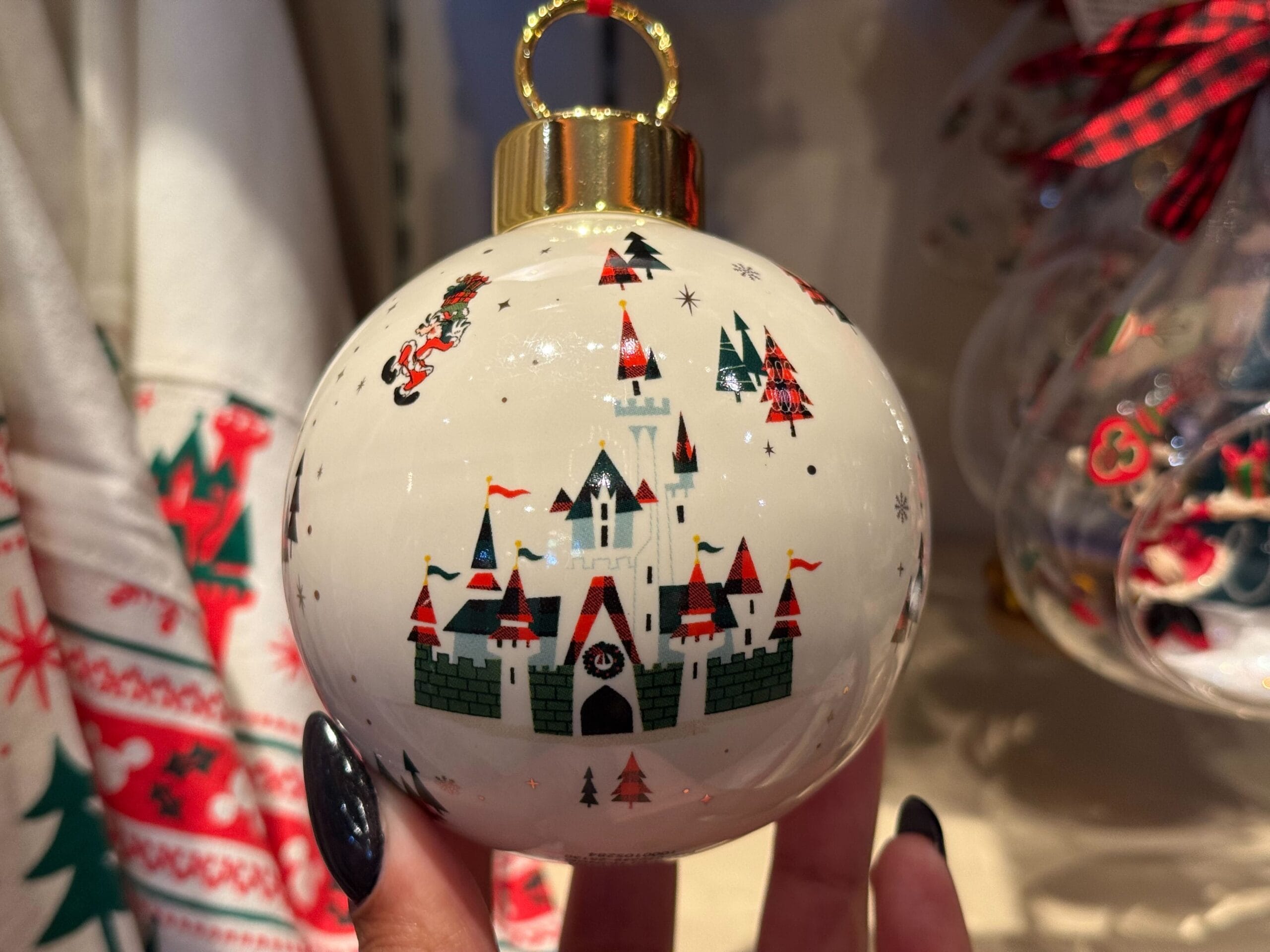 A hand holds a Disneyland Resort Christmas ornament showing a castle—more similar to Anaheim’s than Cinderella Castle—amid holiday decor.