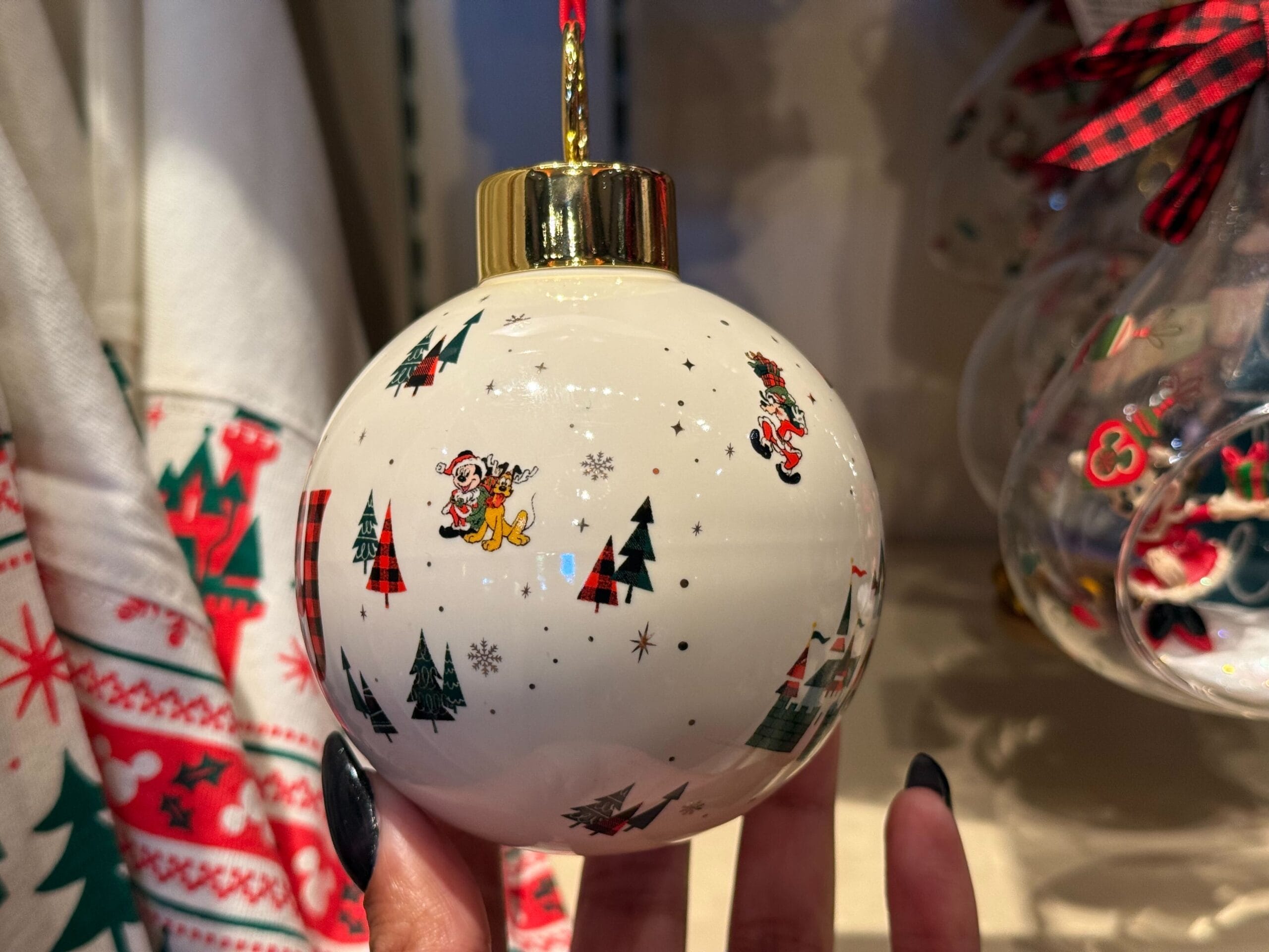 A white Disneyland Resort Christmas ornament with festive trees and cartoon reindeer, held by black nails—no castle in view.