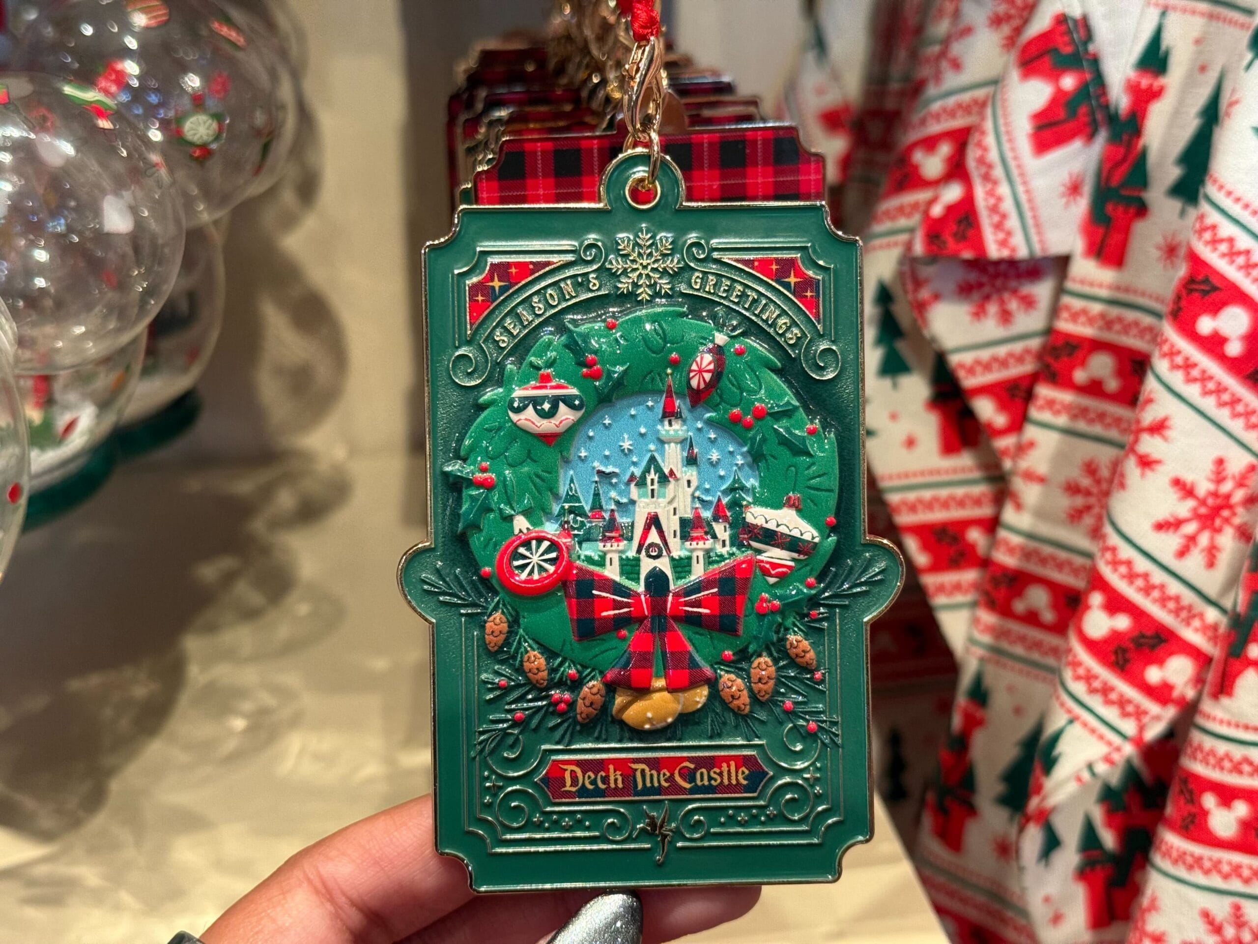 A hand holds a Disneyland Resort Christmas ornament: green with "Season's Greetings" and a castle resembling Sleeping Beauty Castle.