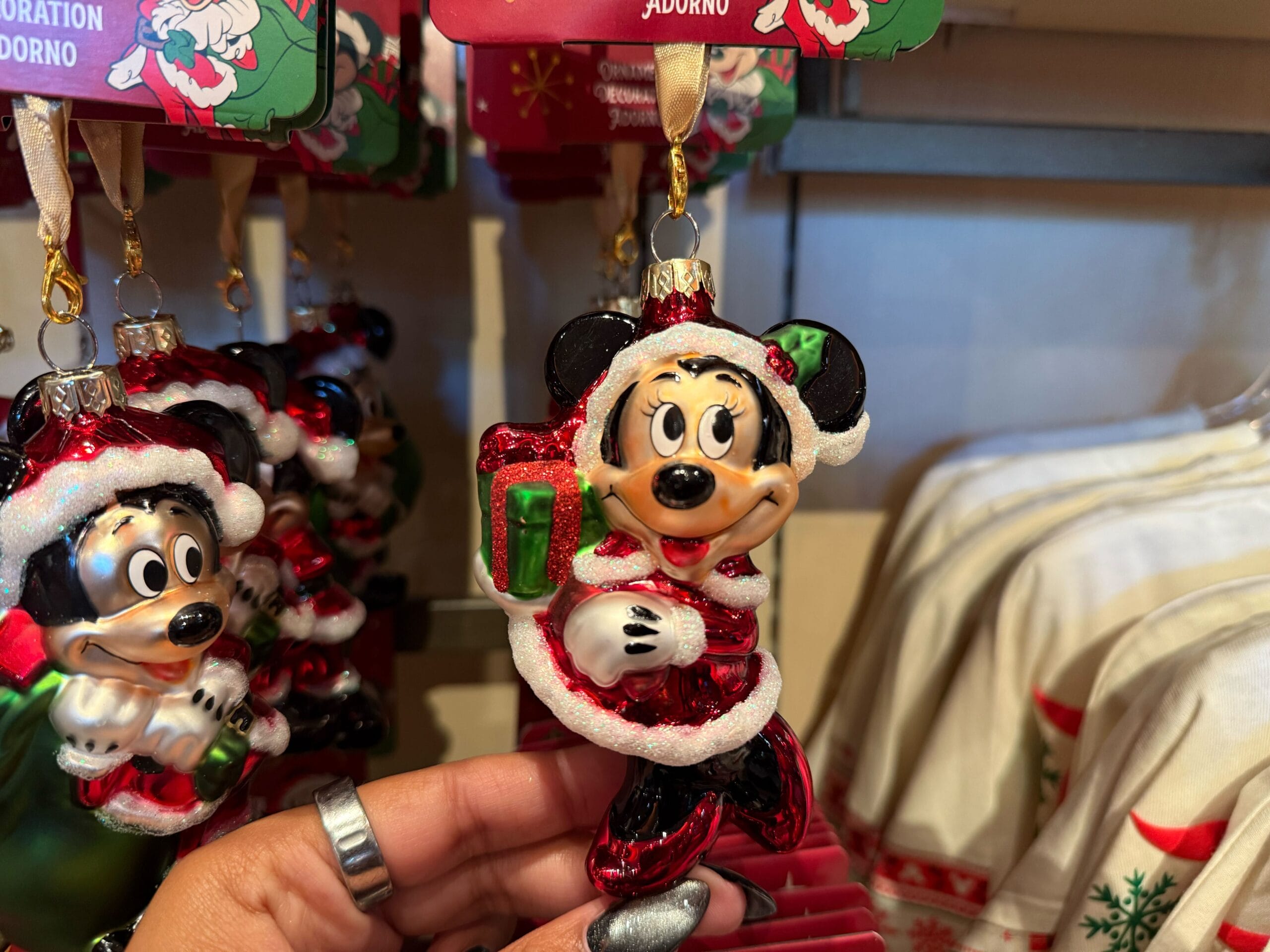 A hand holds a Mickey Mouse Christmas ornament at Disneyland Resort, with festive gifts behind—no castle visible to compare here.