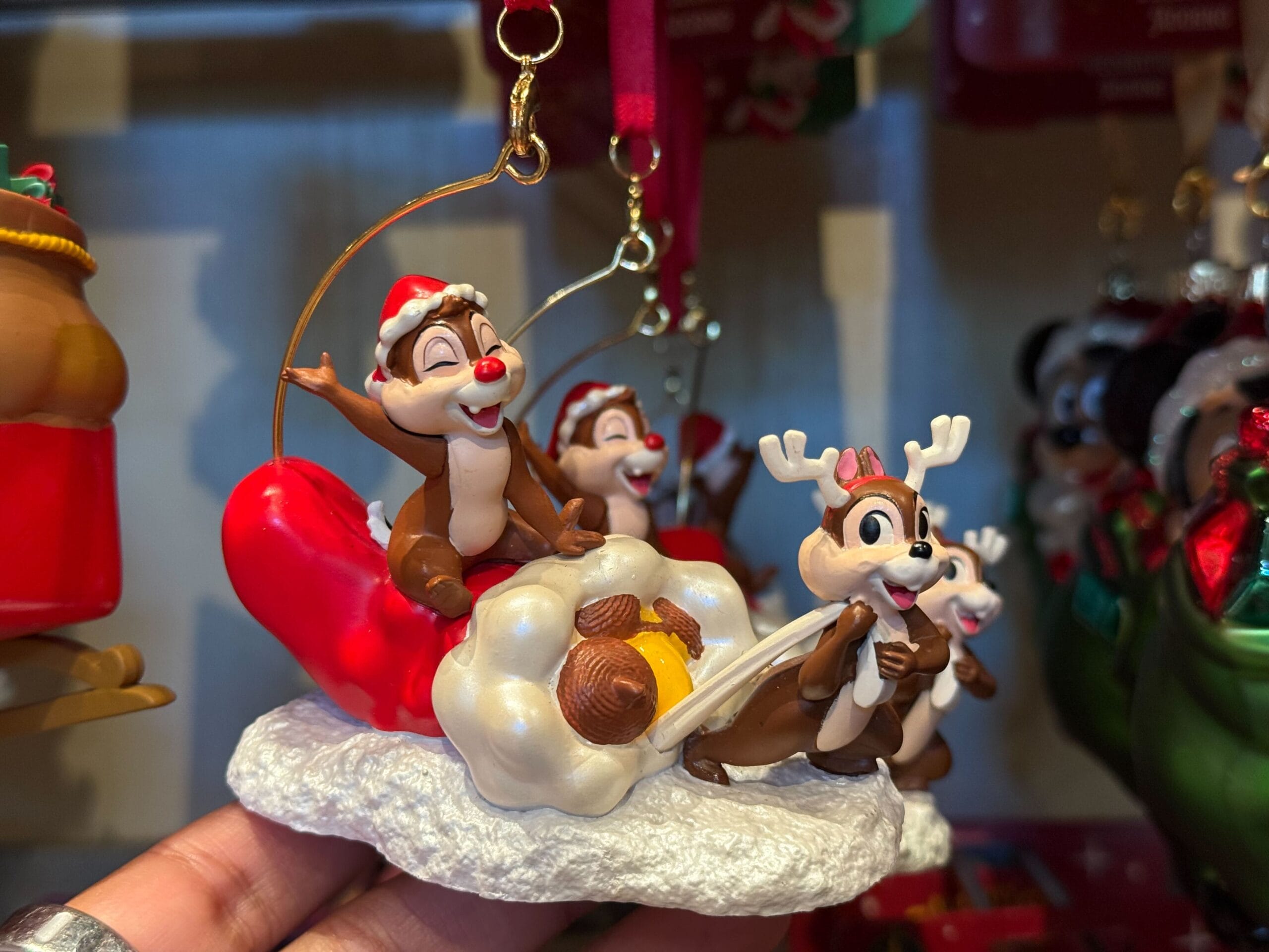 A Disneyland Resort Christmas ornament shows Chip and Dale in festive outfits on a sleigh with acorns, snow, and park-themed details.