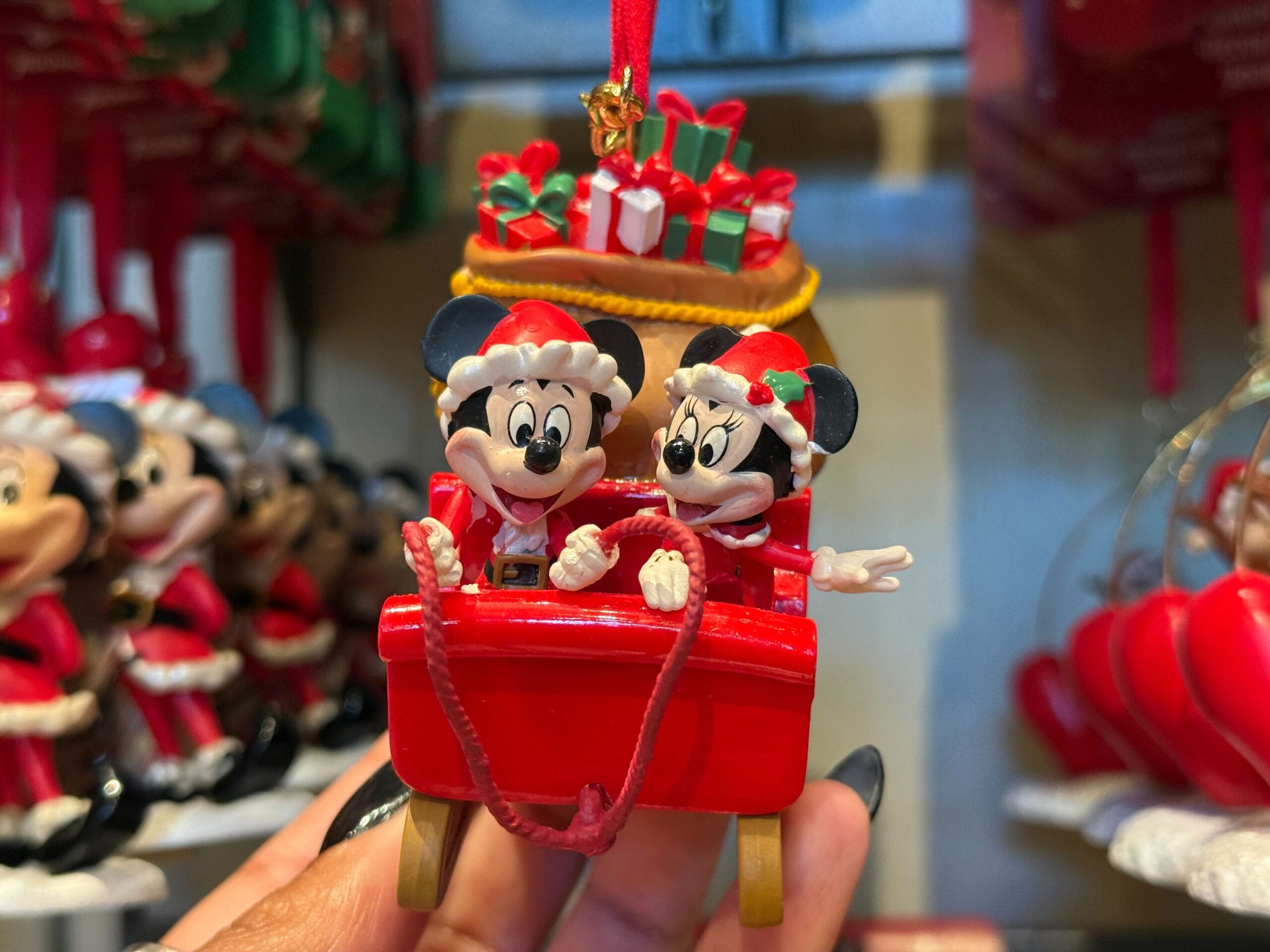 Mickey and Minnie Mouse in Santa hats ride a red sleigh, a Christmas Disneyland ornament; castle not shown for comparison.