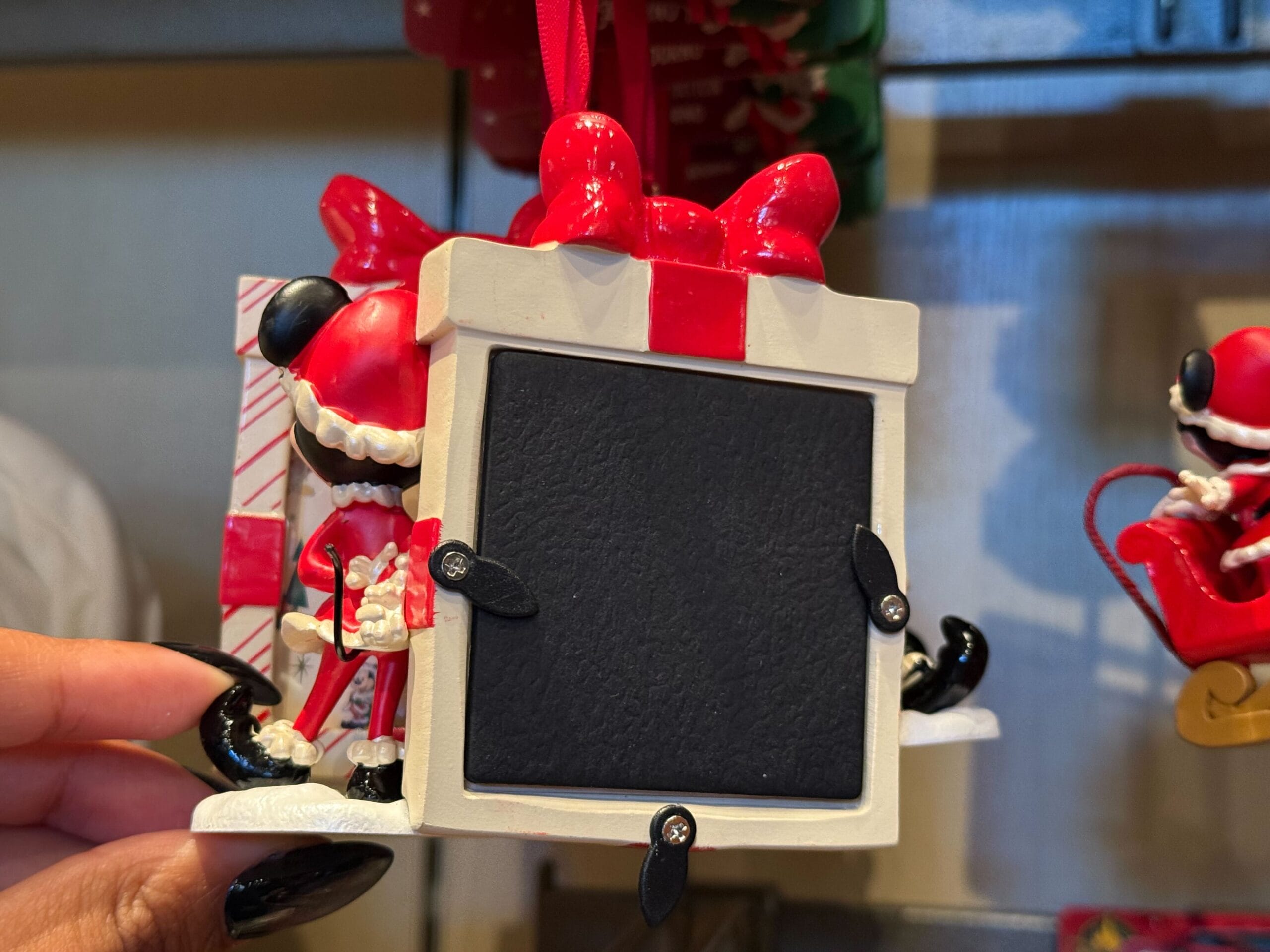 A hand holds a Disneyland Resort Christmas ornament shaped like a gift box with a blank black photo frame, no castle pictured.