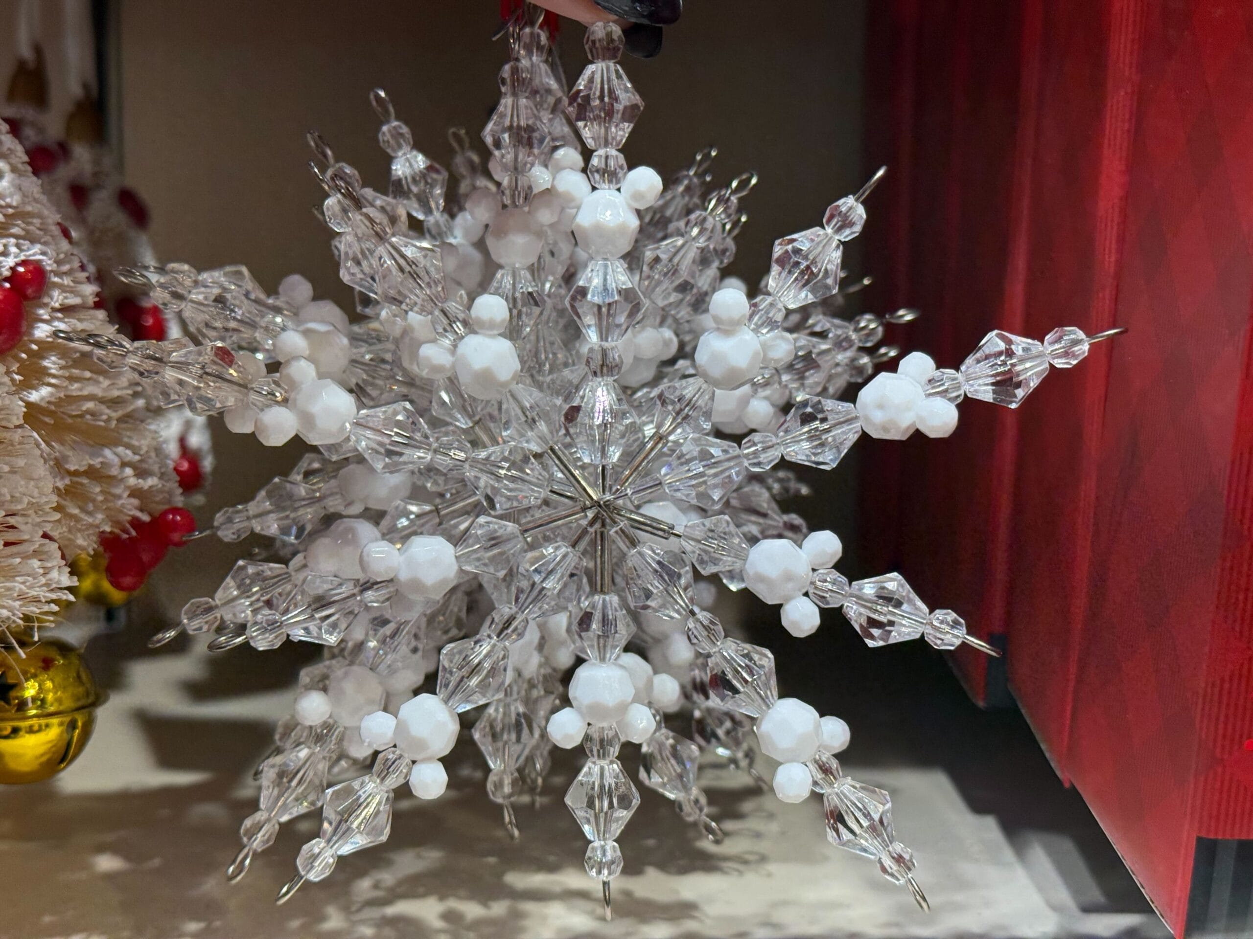 A sparkling clear and white beaded snowflake ornament hangs among festive Disney Parks holiday merchandise, evoking wintry magic.