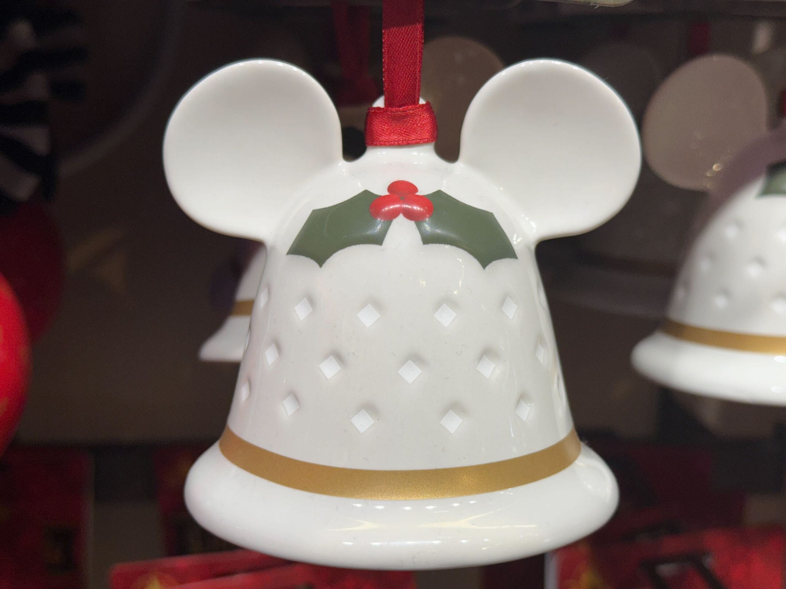 White bell-shaped ornament with mouse ears and holly, part of Disneyland Resort Christmas collection, reminiscent of Sleeping Beauty Castle.