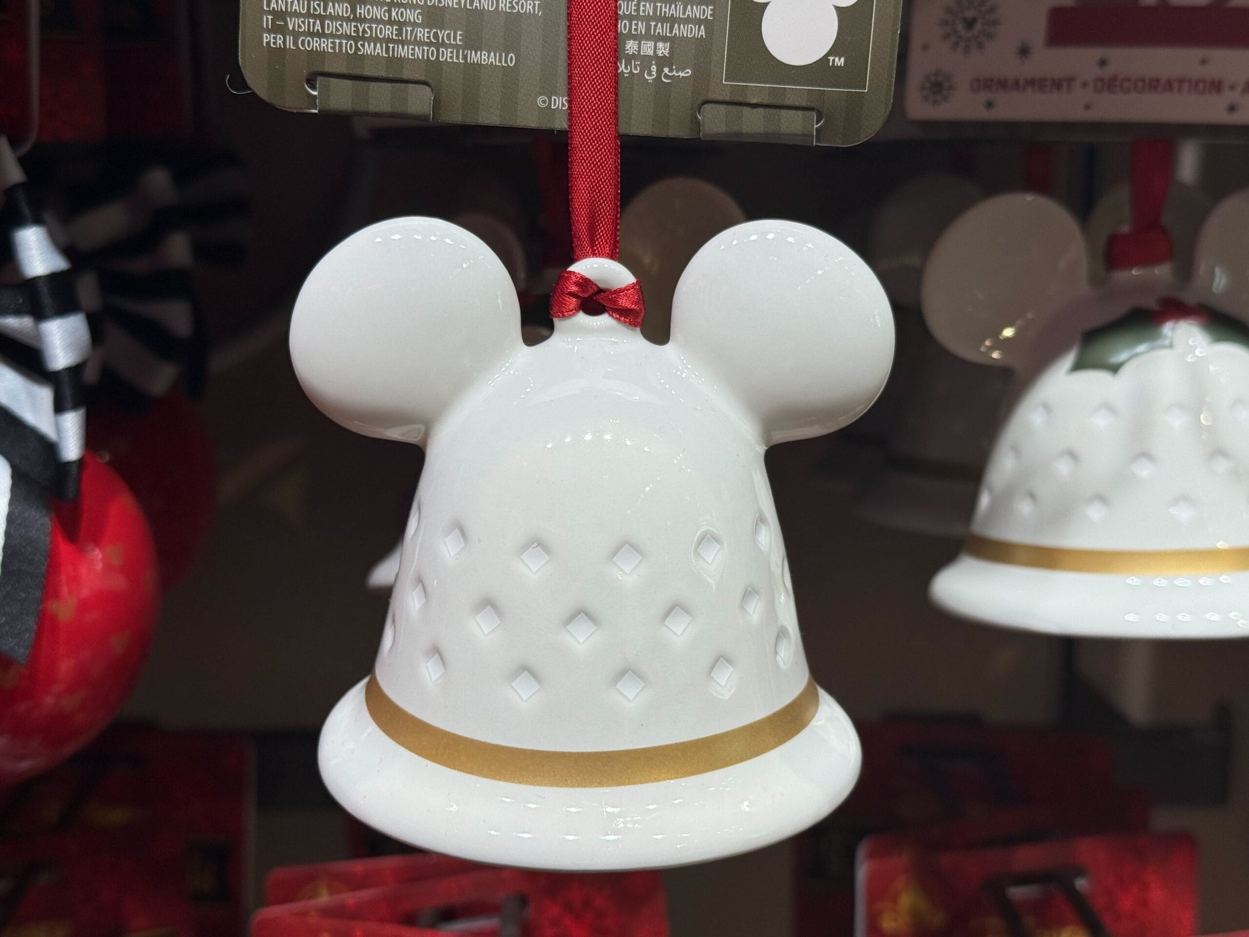White ceramic Mickey mouse head ornament with gold band and red ribbon, part of a festive Disneyland Resort holiday display.