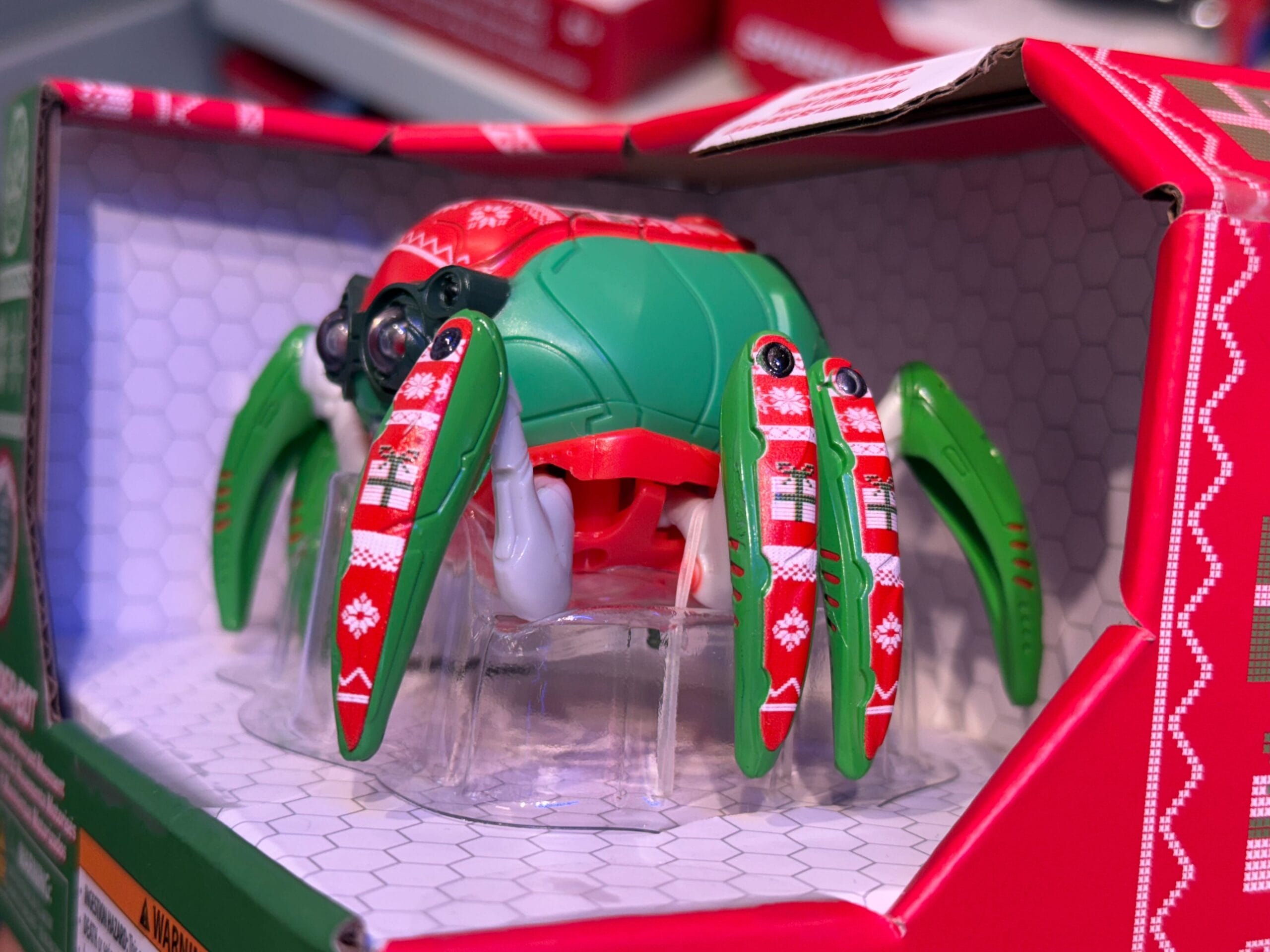 A festive green and red Christmas Spider-Bot with holiday patterns sits in a partially open box at a Disney park gift shop.