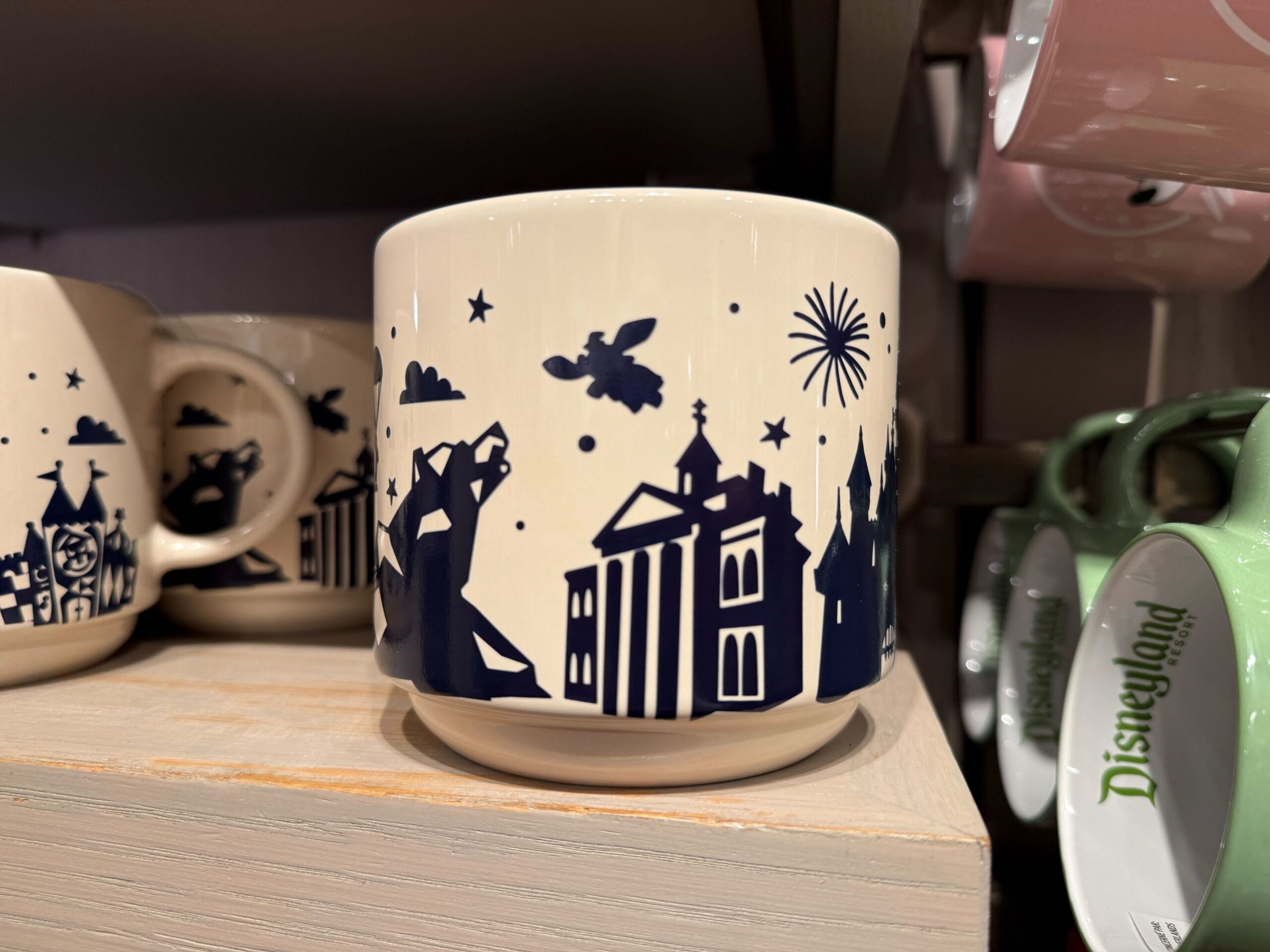 White mug on shelf featuring a navy castle resembling Disneyland’s Sleeping Beauty Castle, fireworks, and Peter Pan in flight.