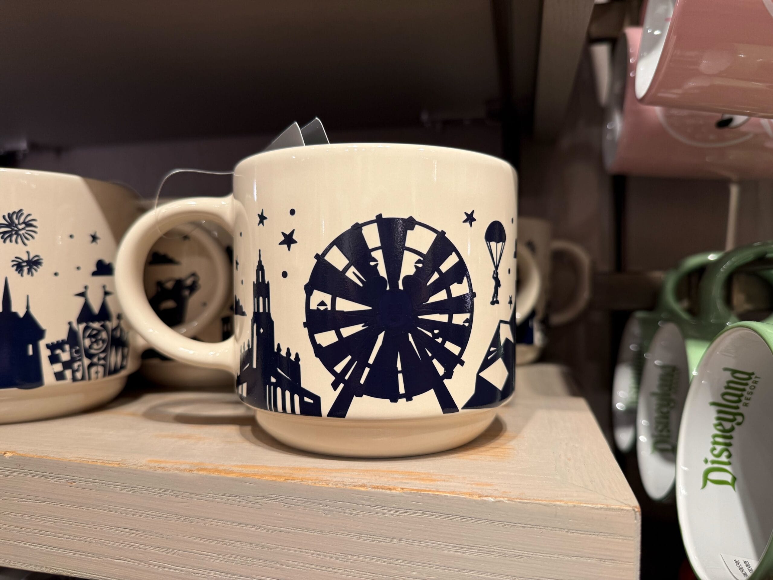Cream mug featuring navy Disney Parks icons—a Ferris wheel reminiscent of California Adventure, hot air balloon, and buildings—on a shelf.