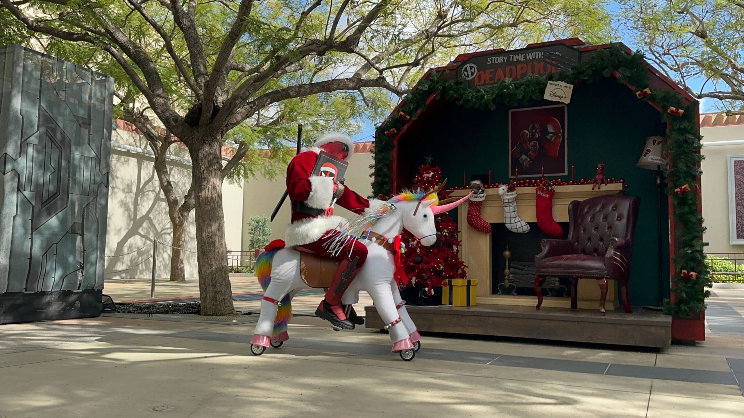A person in a Santa suit rides a fake unicorn at an outdoor Disney holiday display, resembling the festive setups at various Disney parks.