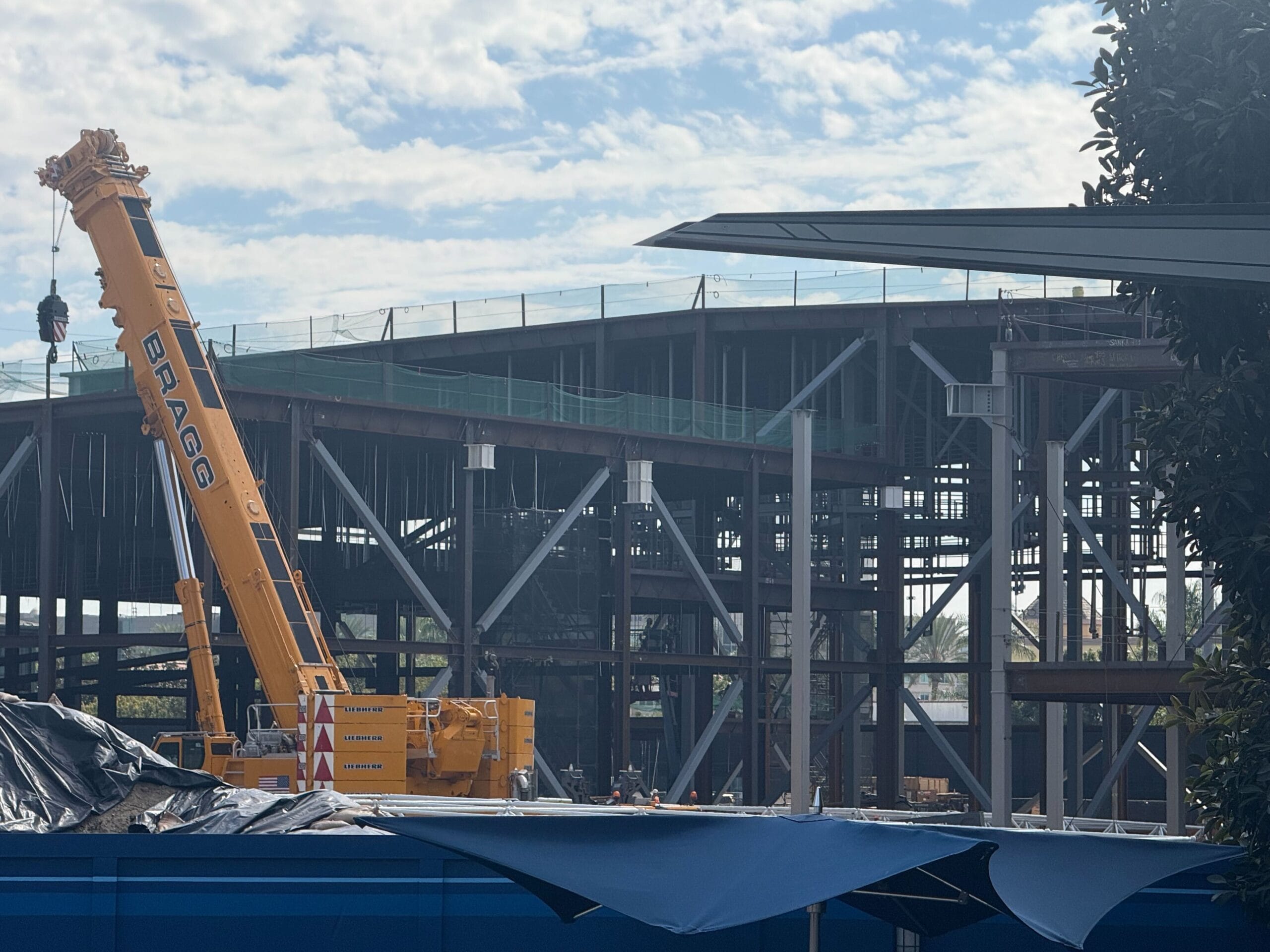 A yellow crane lifts materials at a steel building construction site under a partly cloudy sky, reminiscent of Disneyland park renovations.