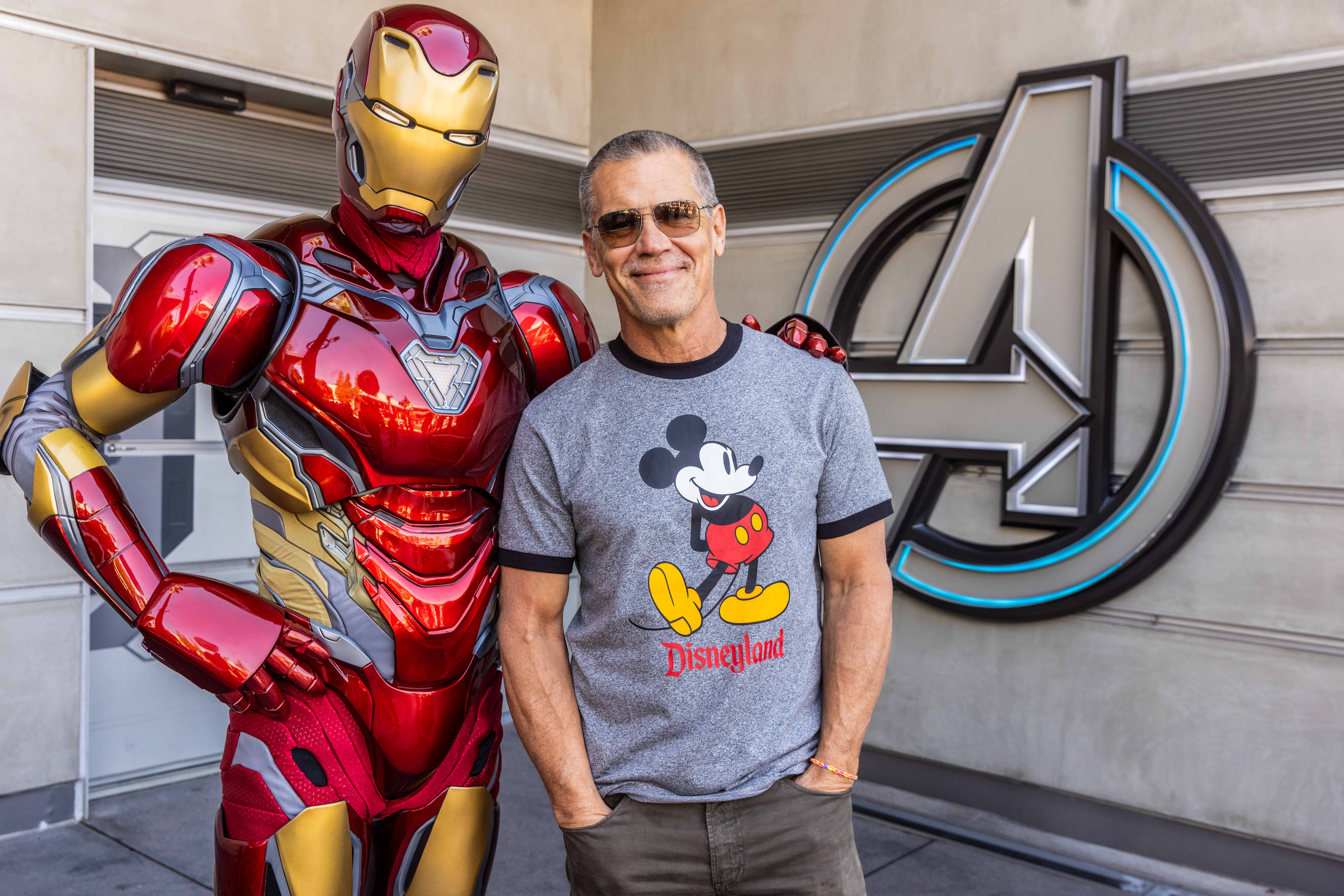 A man poses beside a superhero statue at Avengers Campus in Disney California Adventure, with park details visible in the background.