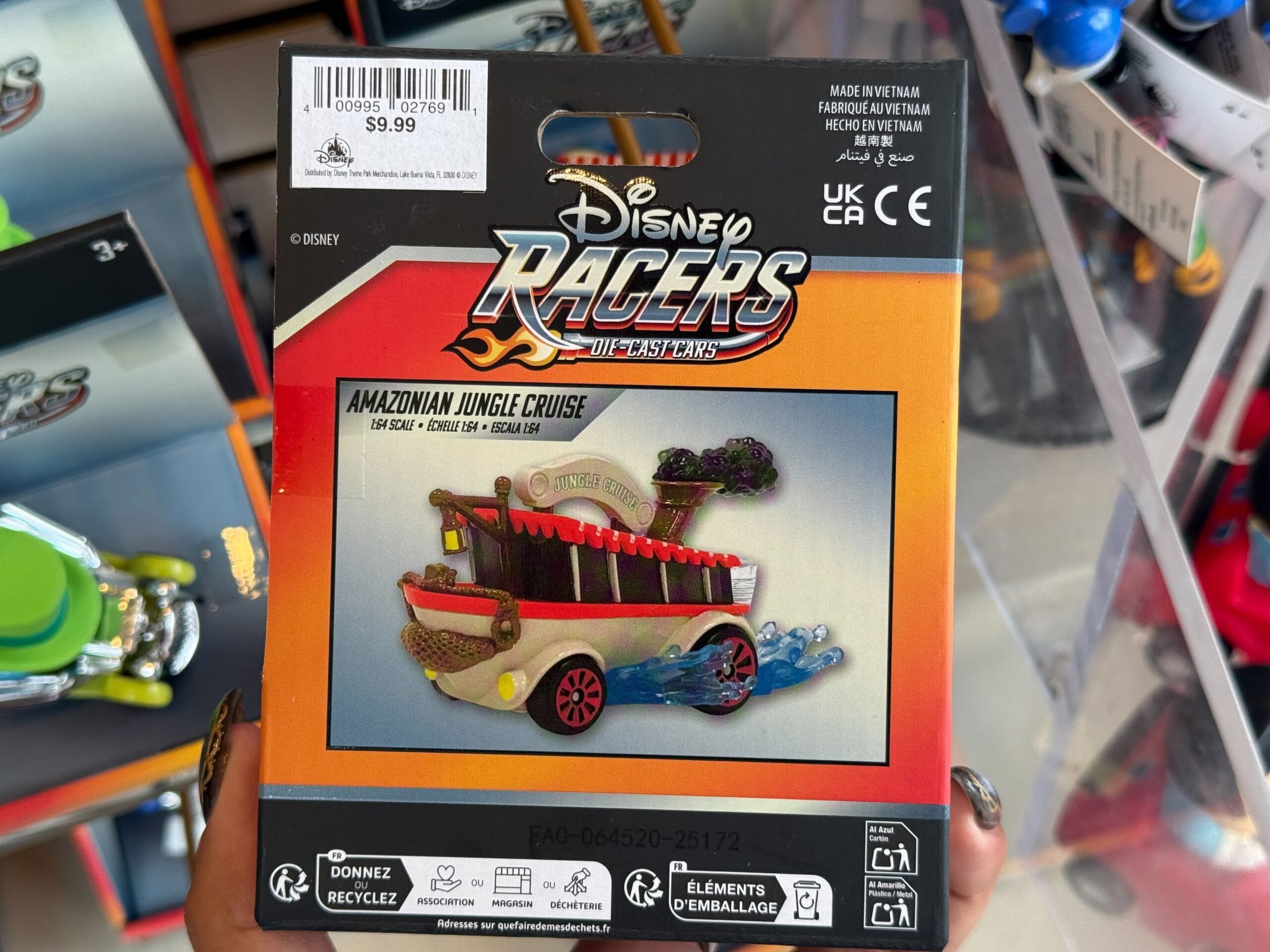 A hand holds a Disney Racers Jungle Cruise car toy package, similar to souvenirs sold at Magic Kingdom, against a colorful backdrop.