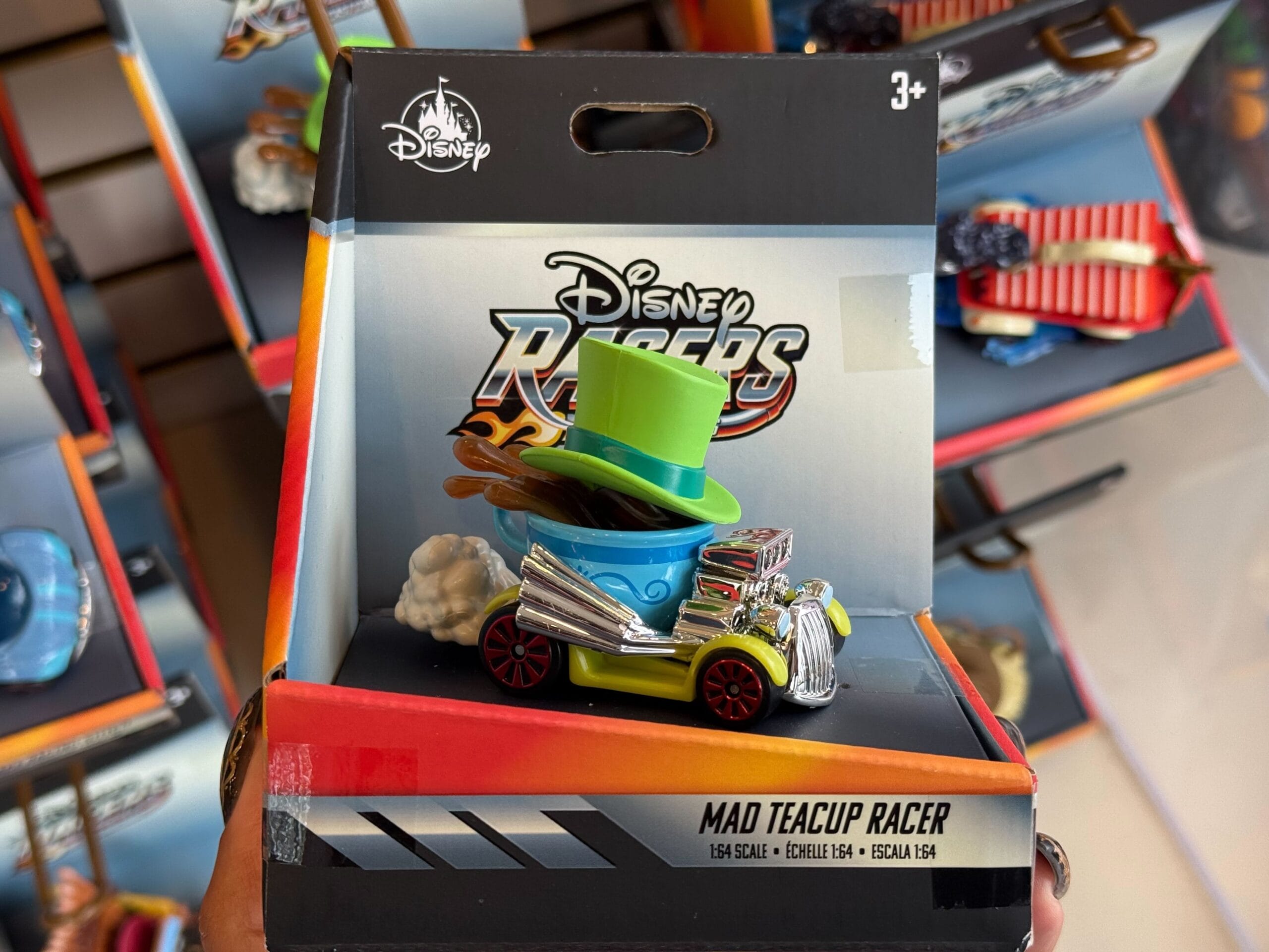 A Disney Racers Mad Teacup racecar toy with a green hat, in Disneyland packaging for ages 3+, reminiscent of park rides.
