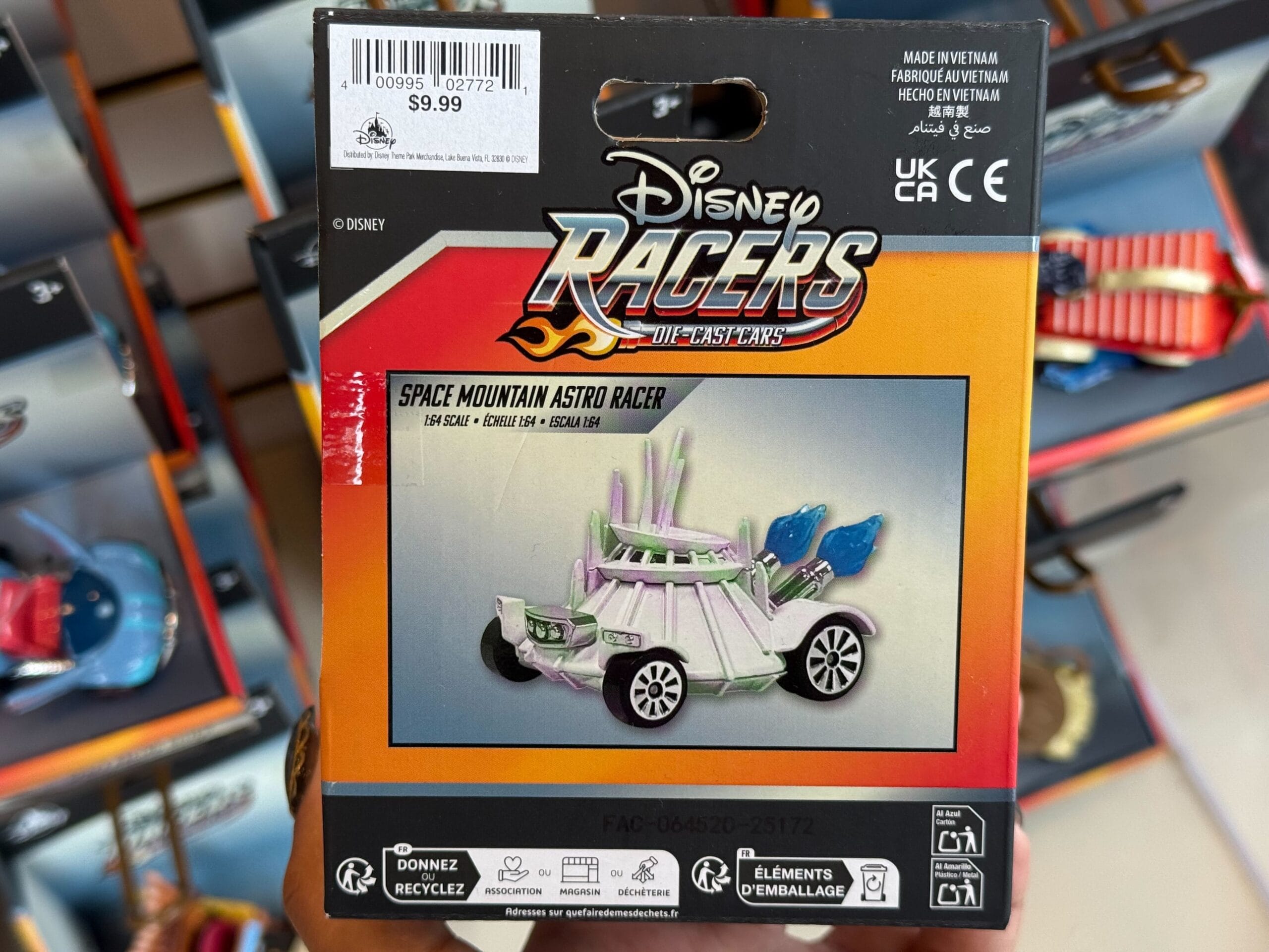 A hand at Disneyland displays a Disney Racers "Space Mountain Astro Racer" toy, price tag $9.99, no castle in sight.