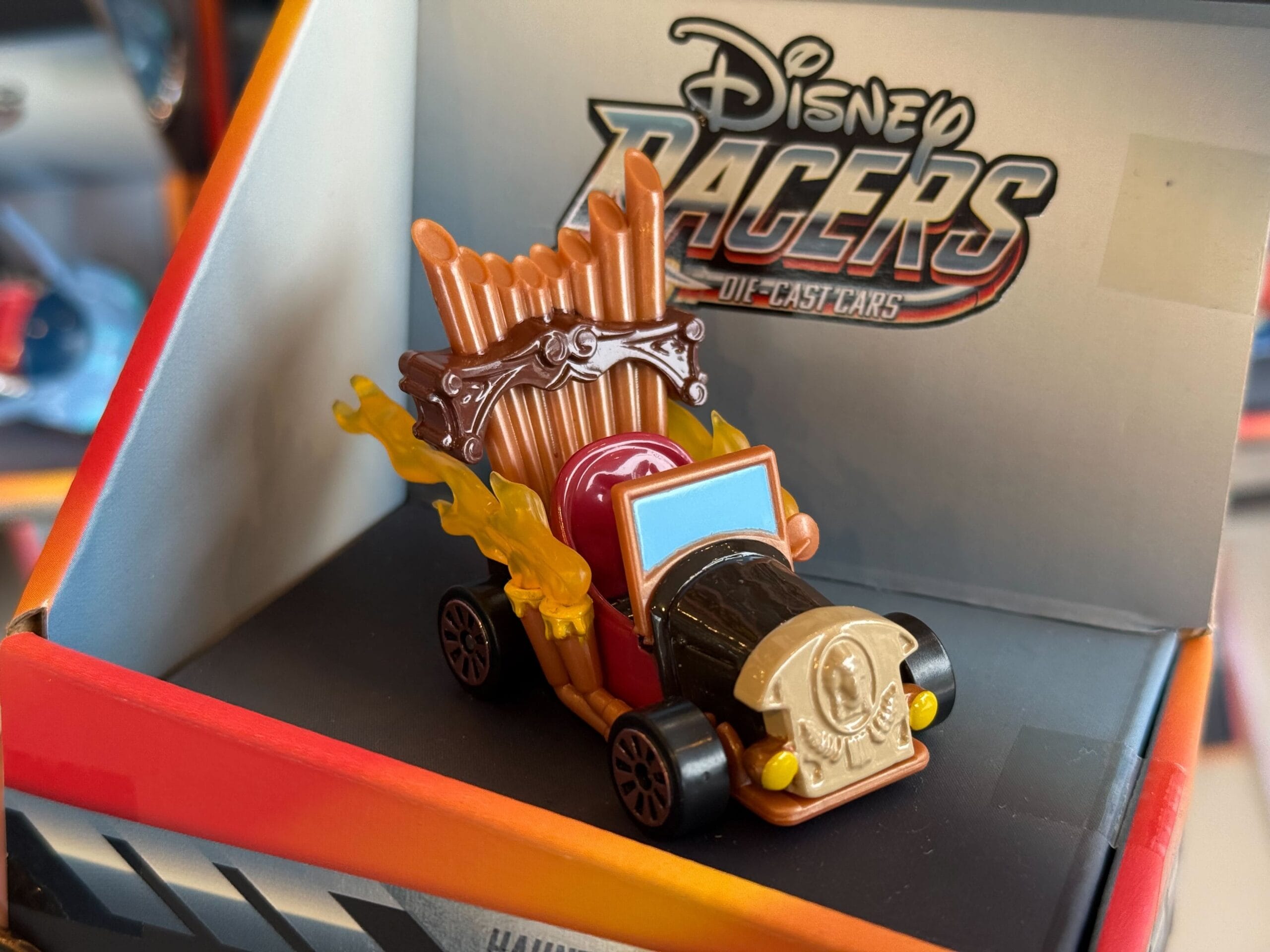 A Disney Racers die-cast car with brown pipes, flames, and a gold emblem, displayed in its box, a classic Disney Parks souvenir.