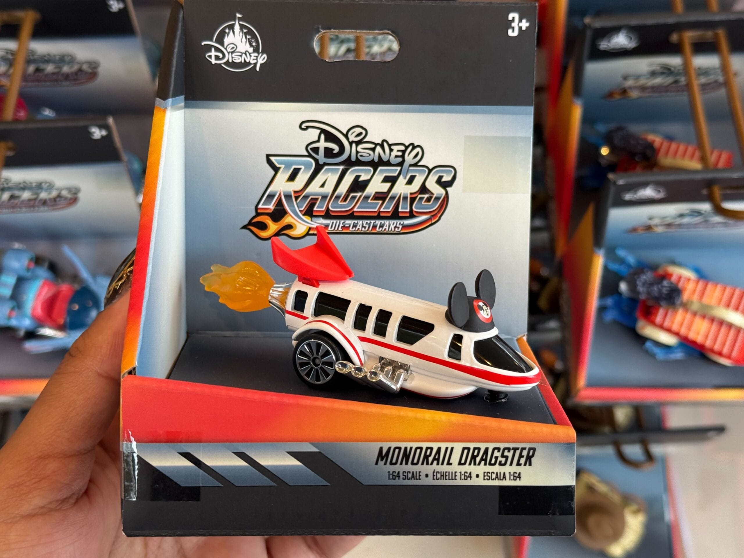A hand displays a Disney Racers Monorail Dragster toy, still boxed, at a Disneyland shop—no castle in view for comparison.