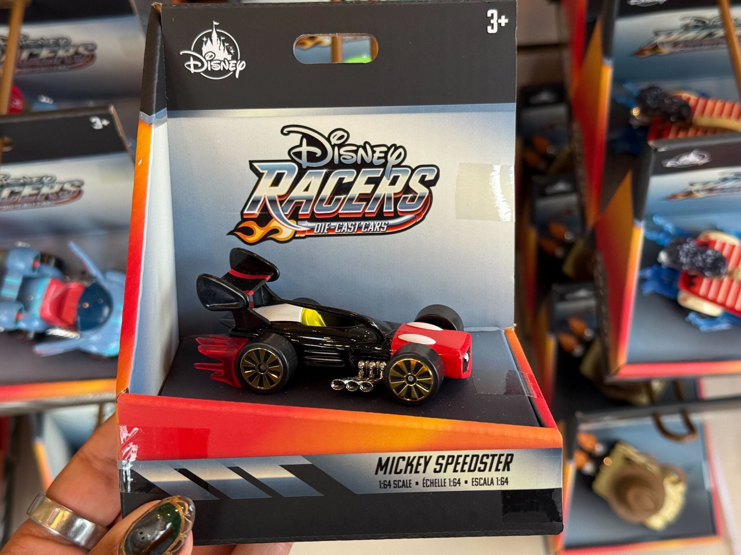 A packaged Disney Racers "Mickey Speedster" toy car on a store shelf, often found in Disney Parks shops near castle displays.