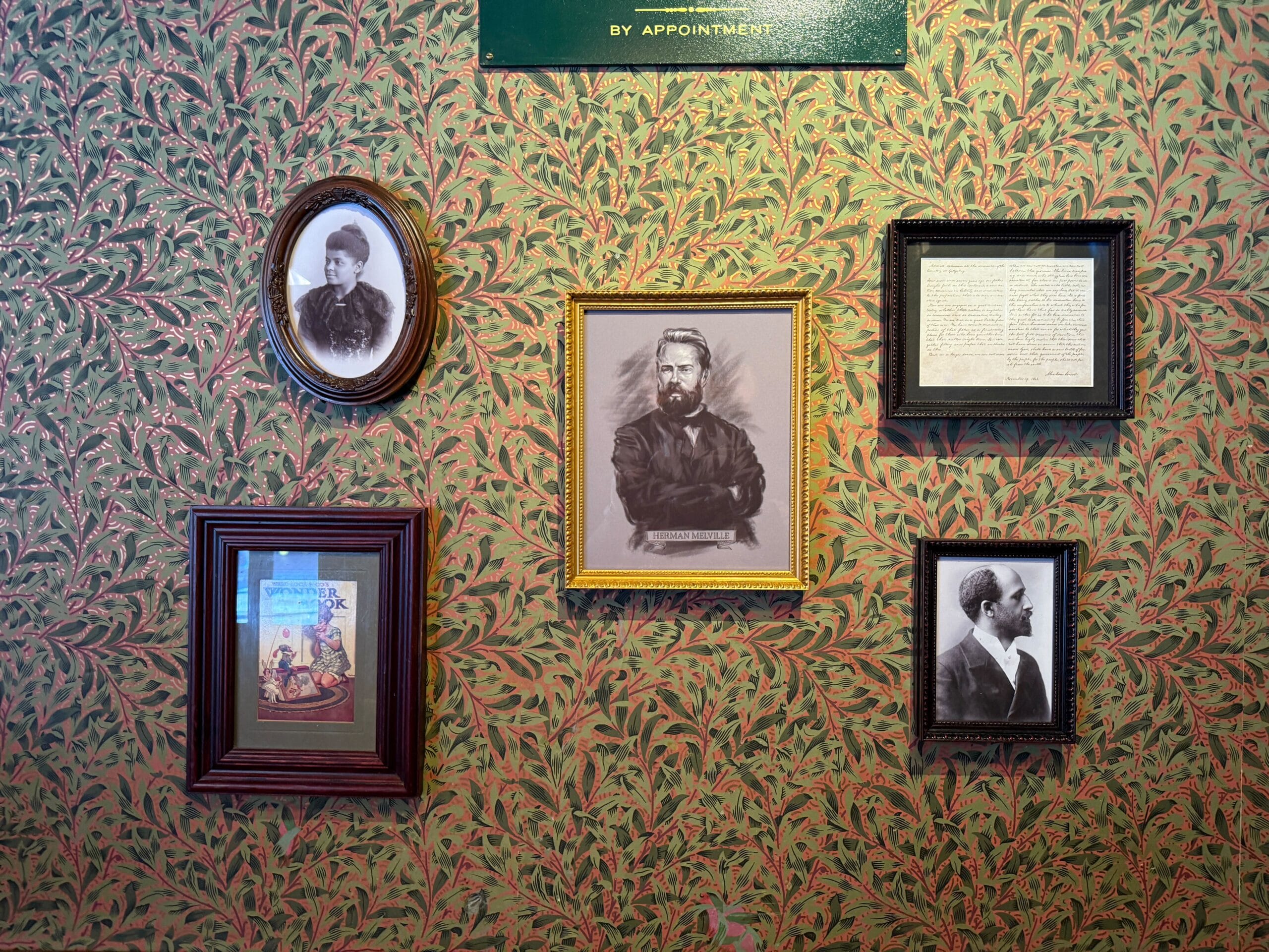 Five framed Disney park photos and documents hang on patterned green and red wallpaper; one castle resembles Disneyland Paris.