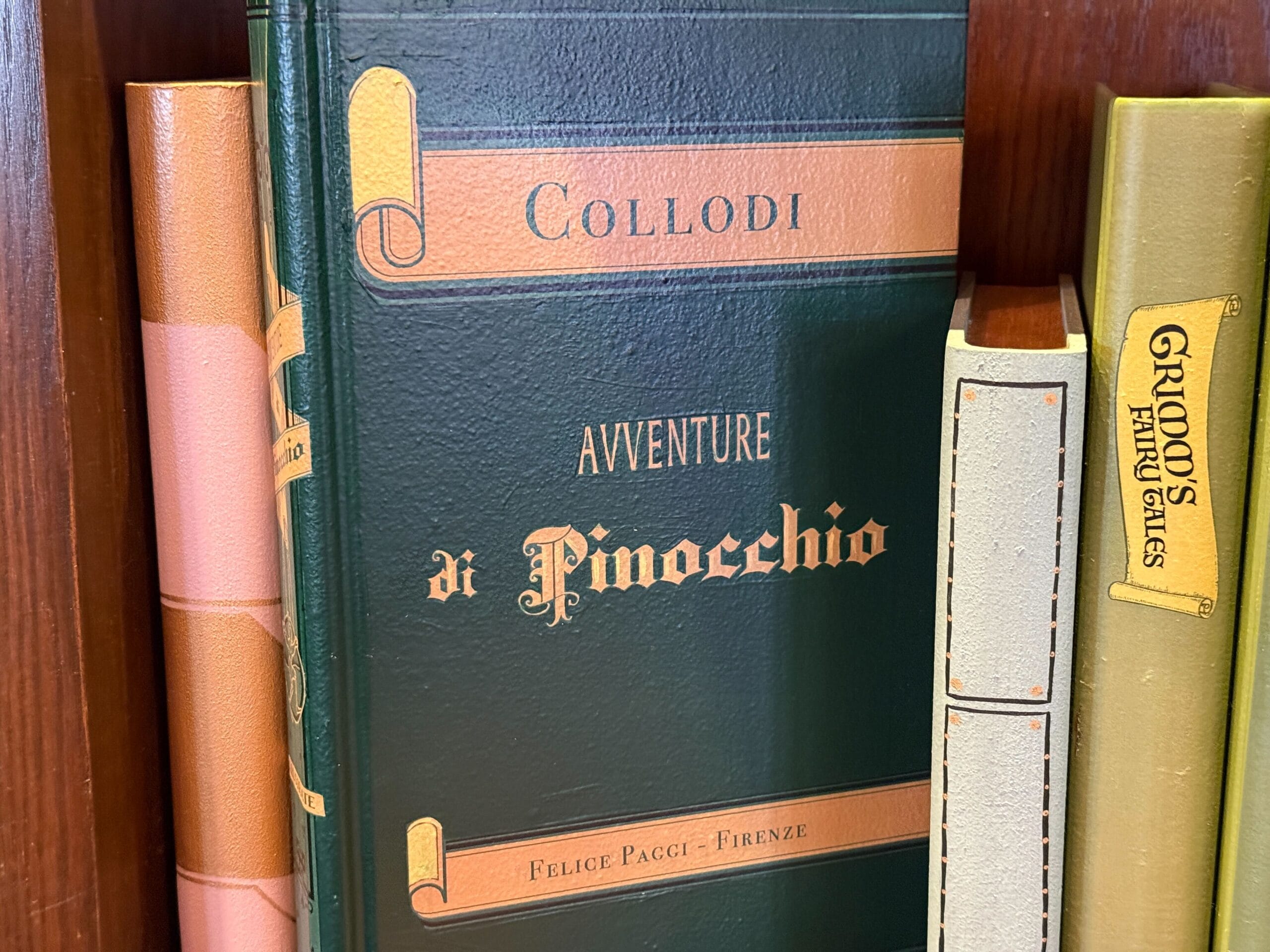Green "Avventure di Pinocchio" book by Collodi on a shelf, surrounded by other books like you'd find in Fantasyland at Disney parks.