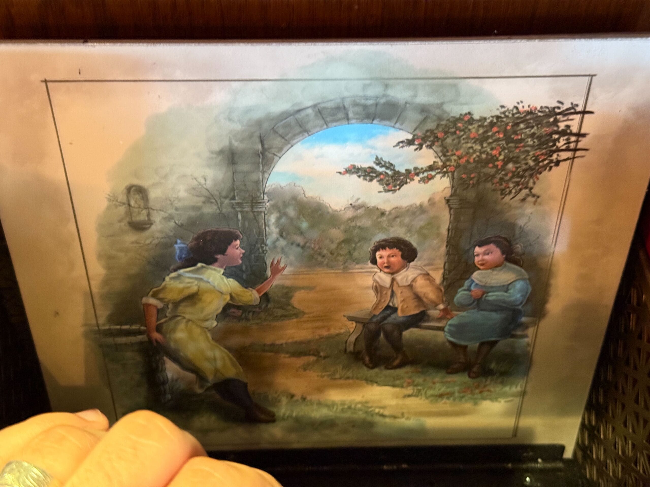 Three children by a stone gate; two sit on a bench like at Disneyland's Fantasyland, one stands reaching toward them.