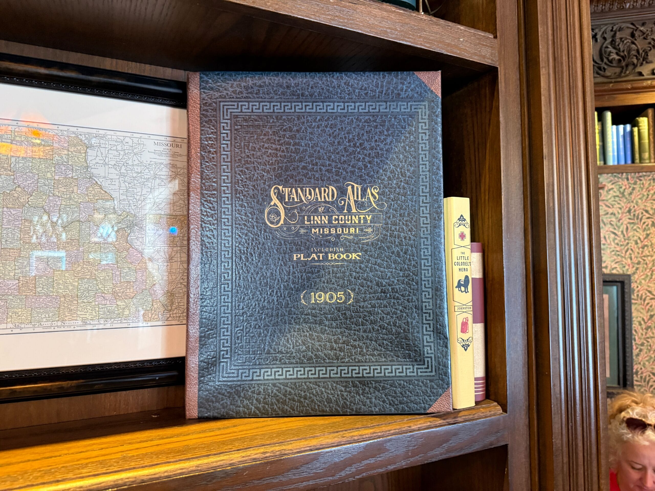 A vintage 1905 plat book, "Standard Atlas of Linn County Missouri," stands upright on a wooden shelf—no Disney castle in sight.