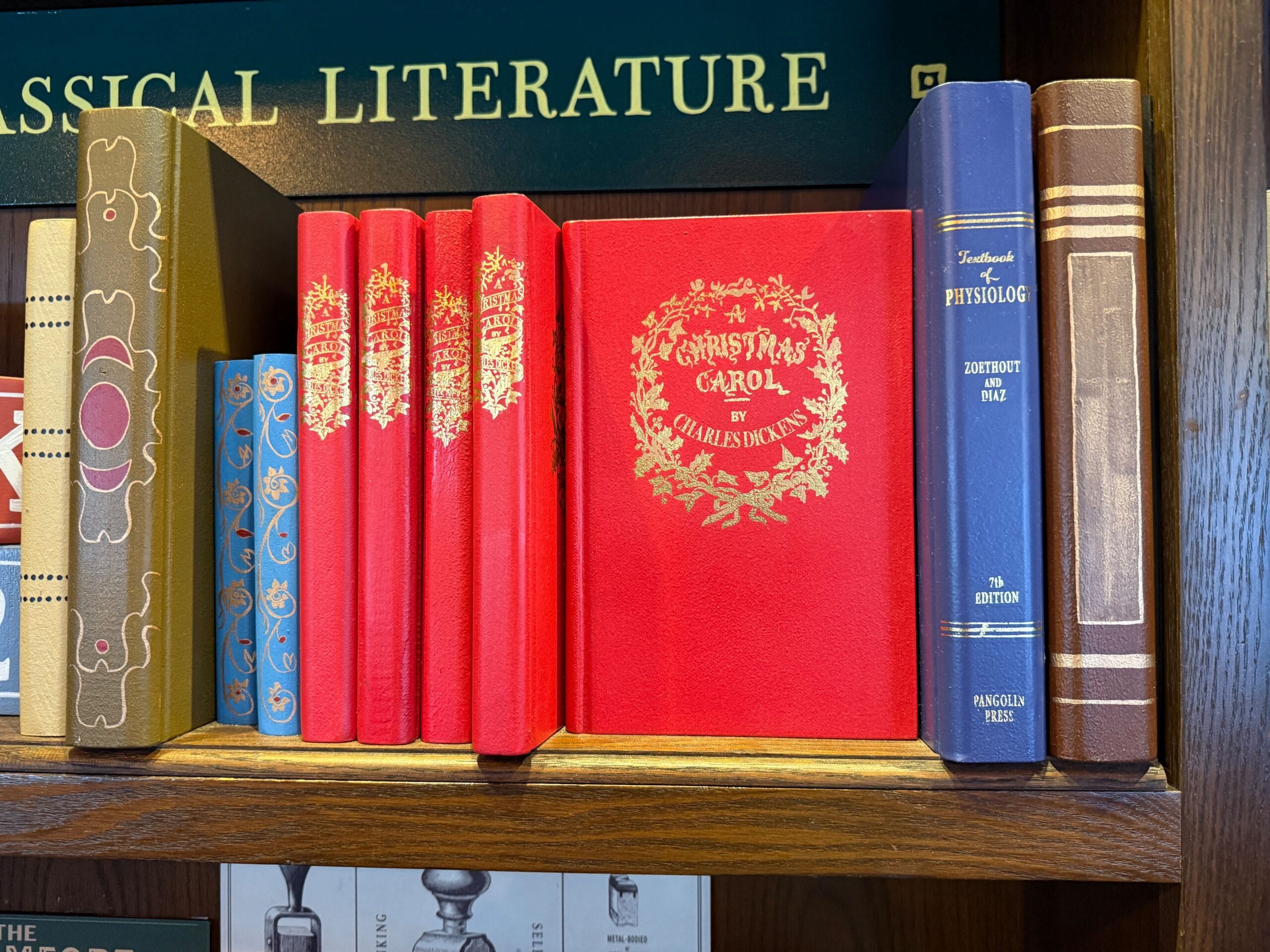 A bookshelf with classic books, including "A Christmas Carol" in bright red and gold, styled like Main Street U.S.A. shop displays.