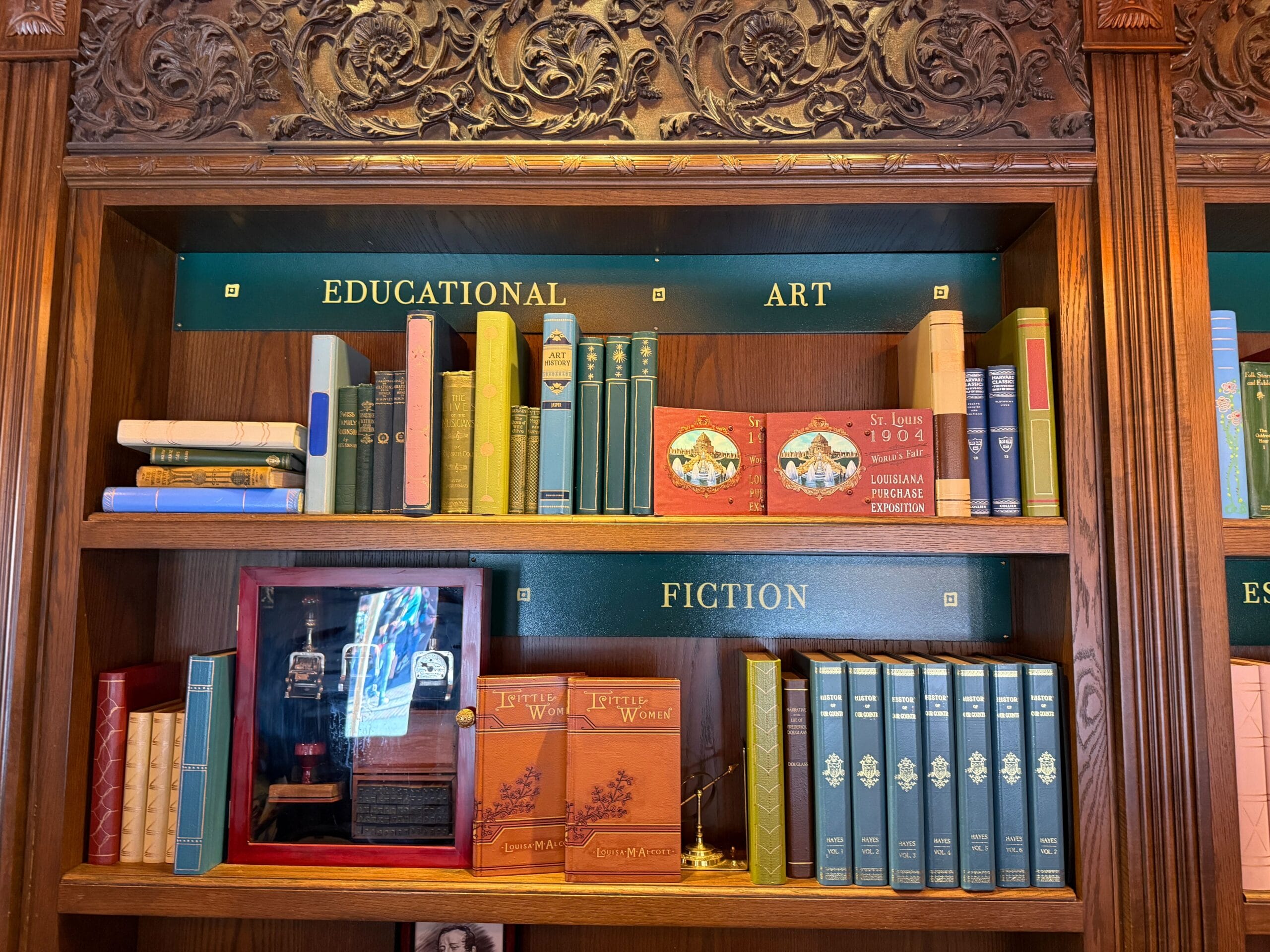 Books are lined up on wooden shelves labeled "EDUCATIONAL ART" and "FICTION," with decorative woodwork reminiscent of Disney parks.