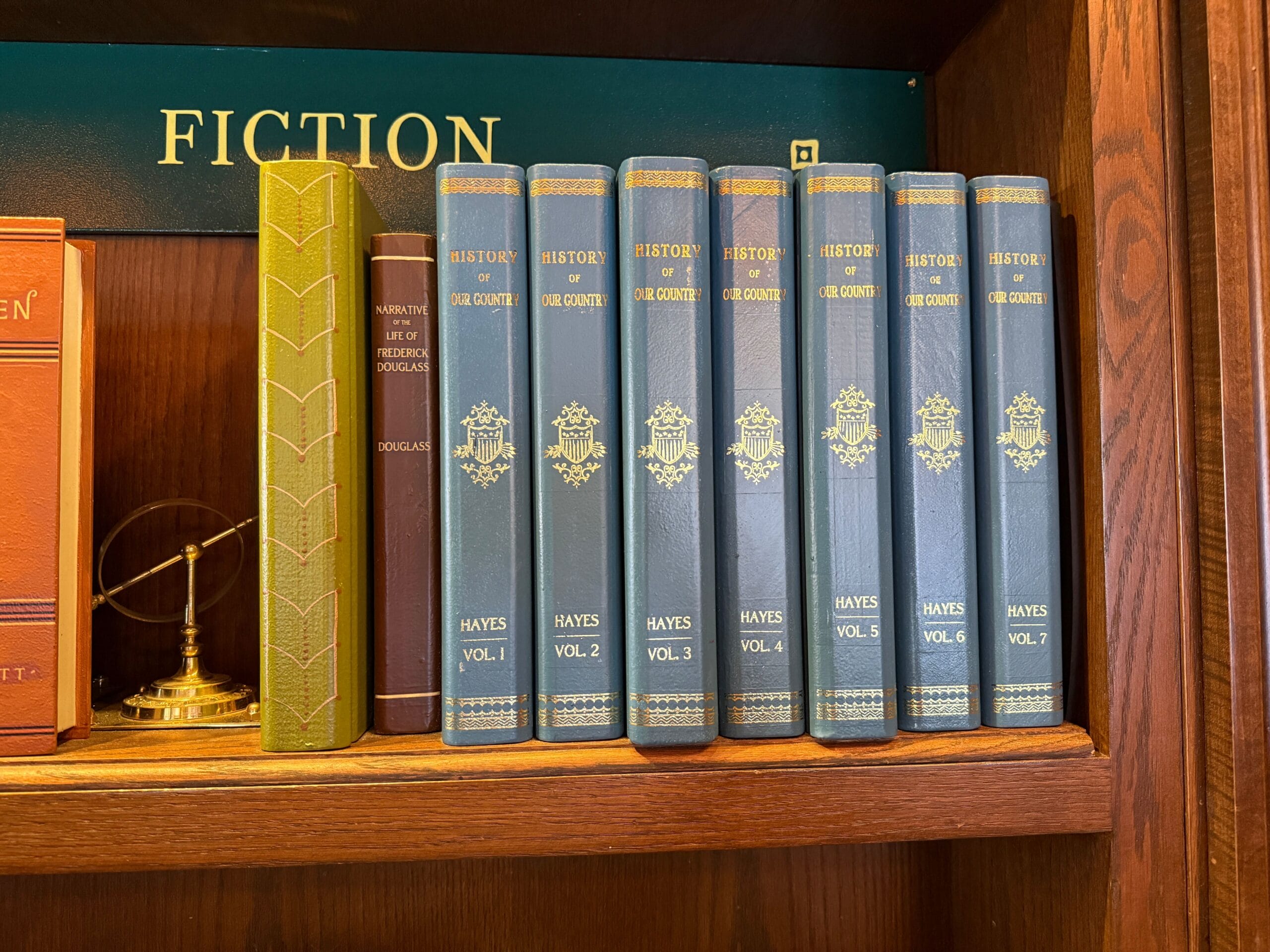 Seven blue "History of Our Country" books by Hayes on a shelf labeled "Fiction," like Main Street shops in Disney parks.