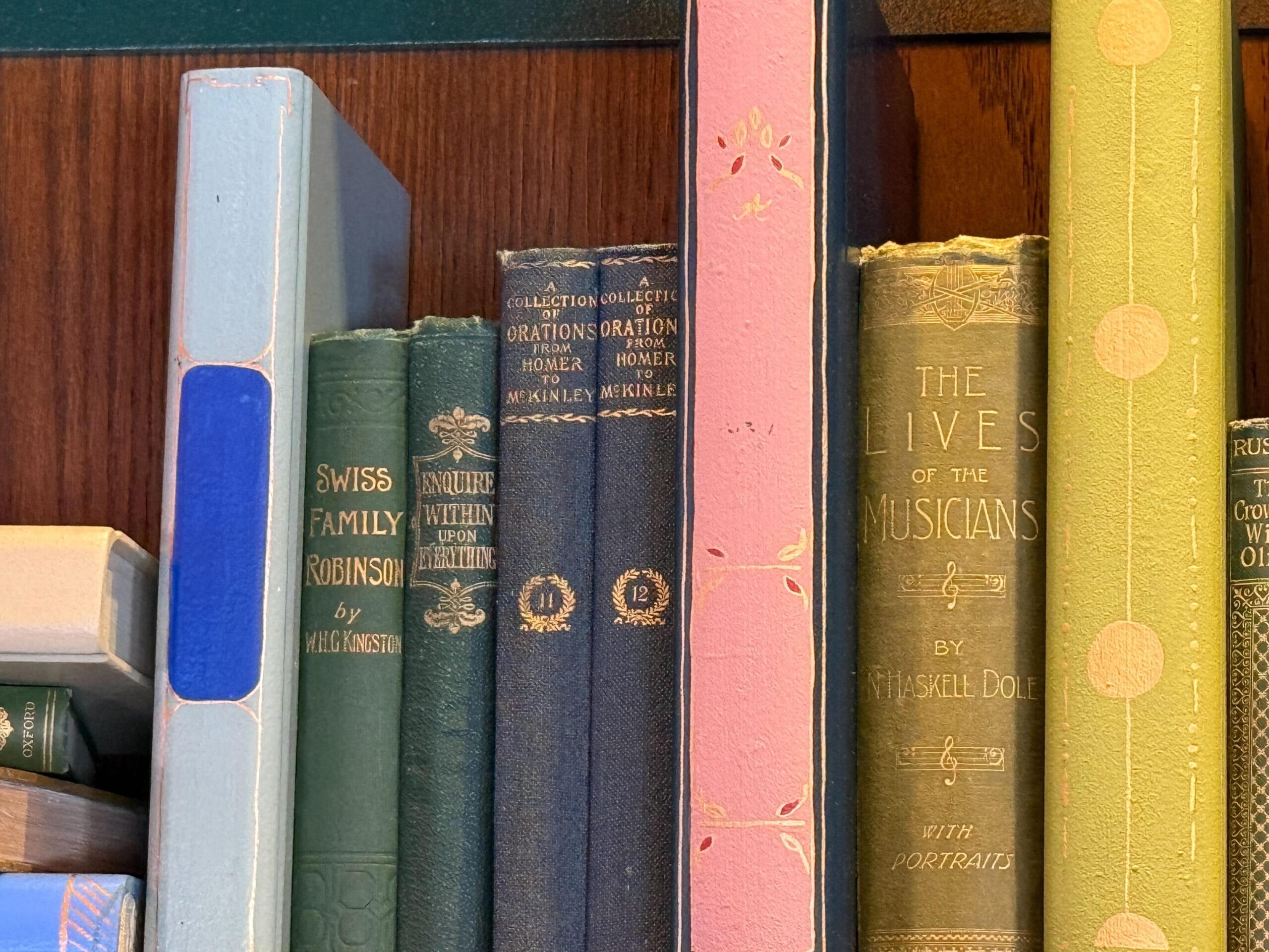 Close-up of vintage books on a shelf, featuring "Swiss Family Robinson" and "The Lives of the Musicians," evoking Disney park libraries.