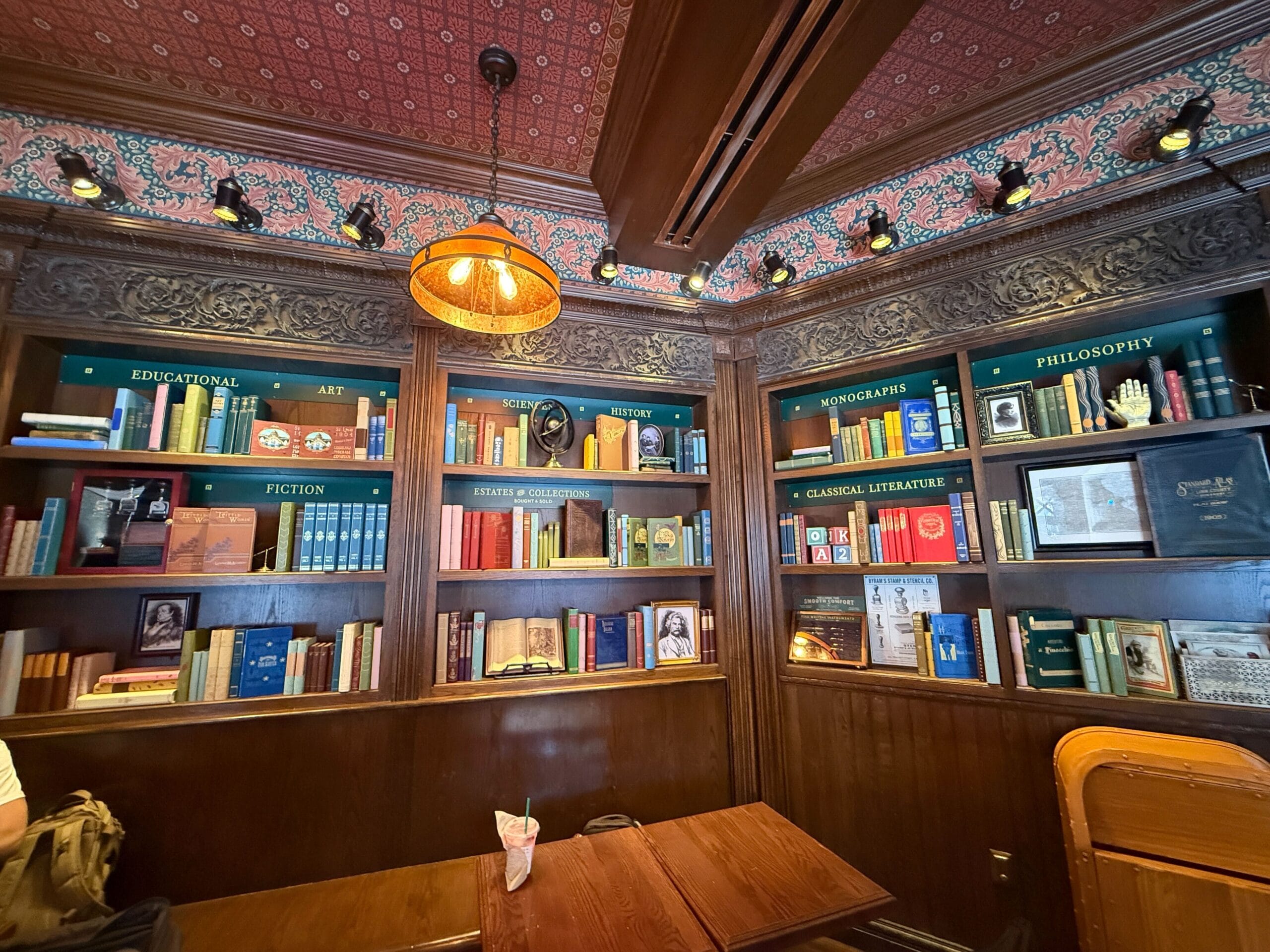 Wood-paneled library with shelves, books, and décor; table and chairs under a lamp, reminiscent of Disney park fantasy interiors.