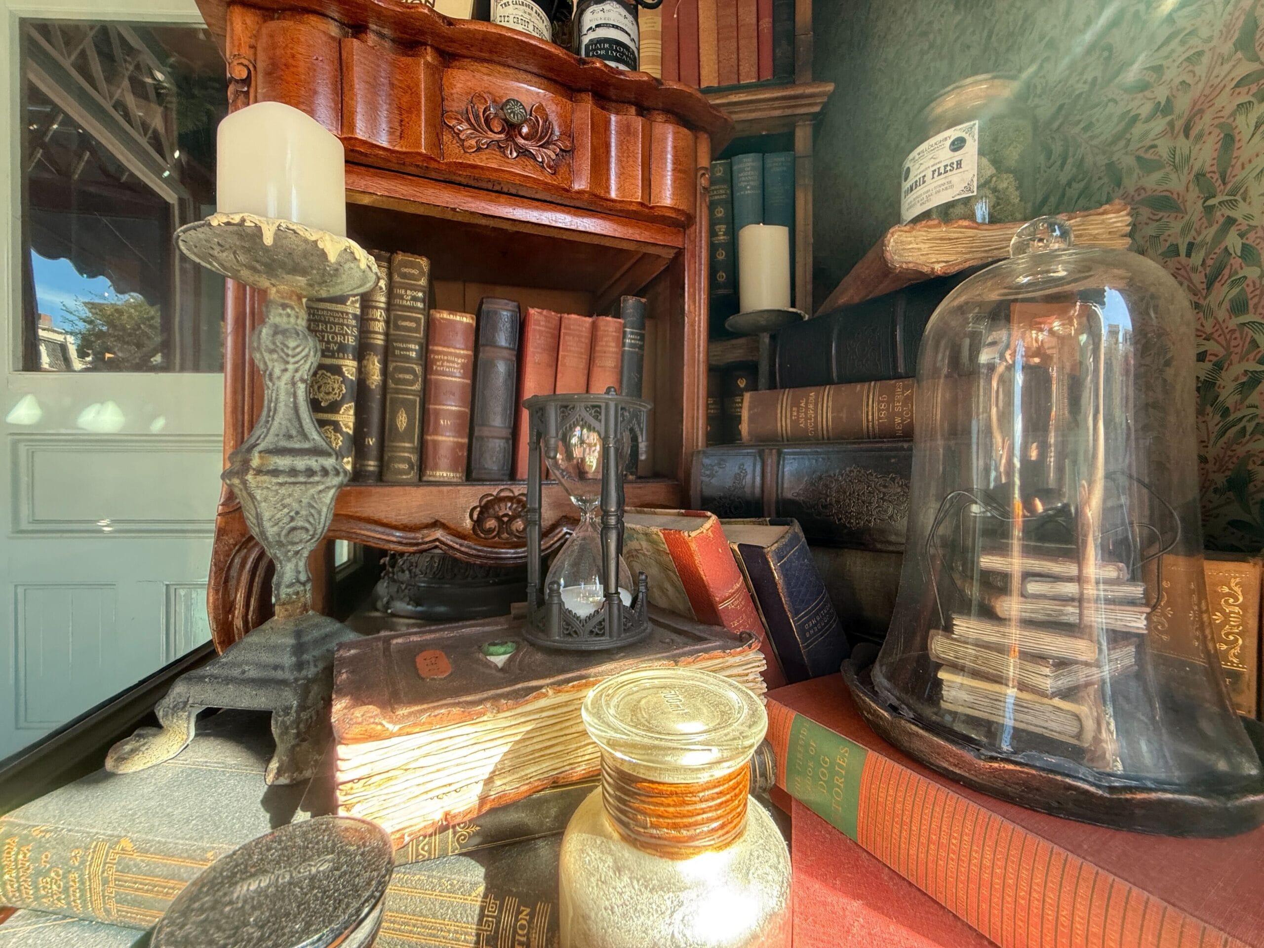A cozy vintage study, like a nook in Disneyland’s Liberty Square, with old books, an hourglass, candles, and jars on a sunlit desk.