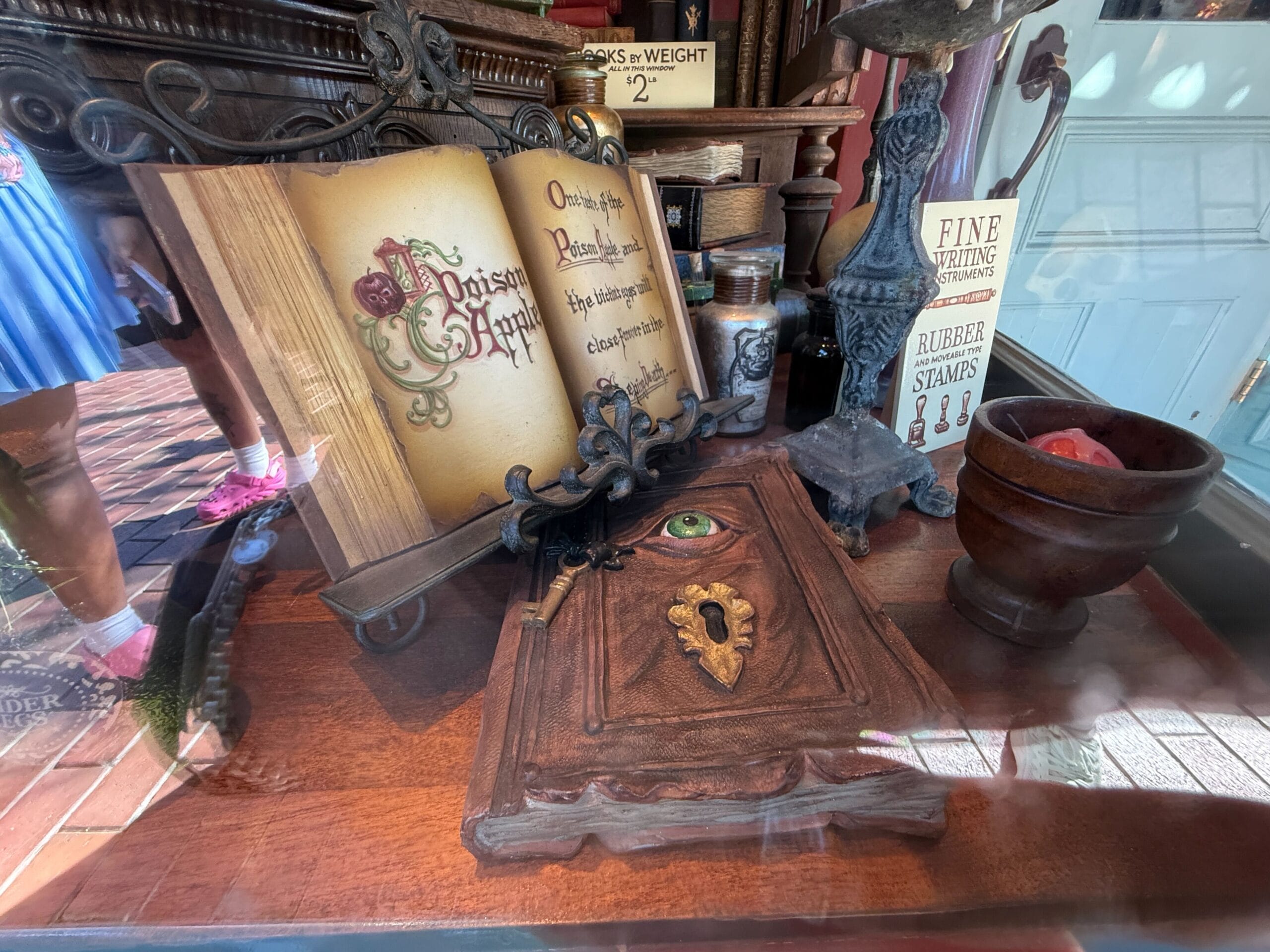 A decorative "Poison Apple" book sits open next to a wooden box with a green eye, like an artifact from a Disney parks display.