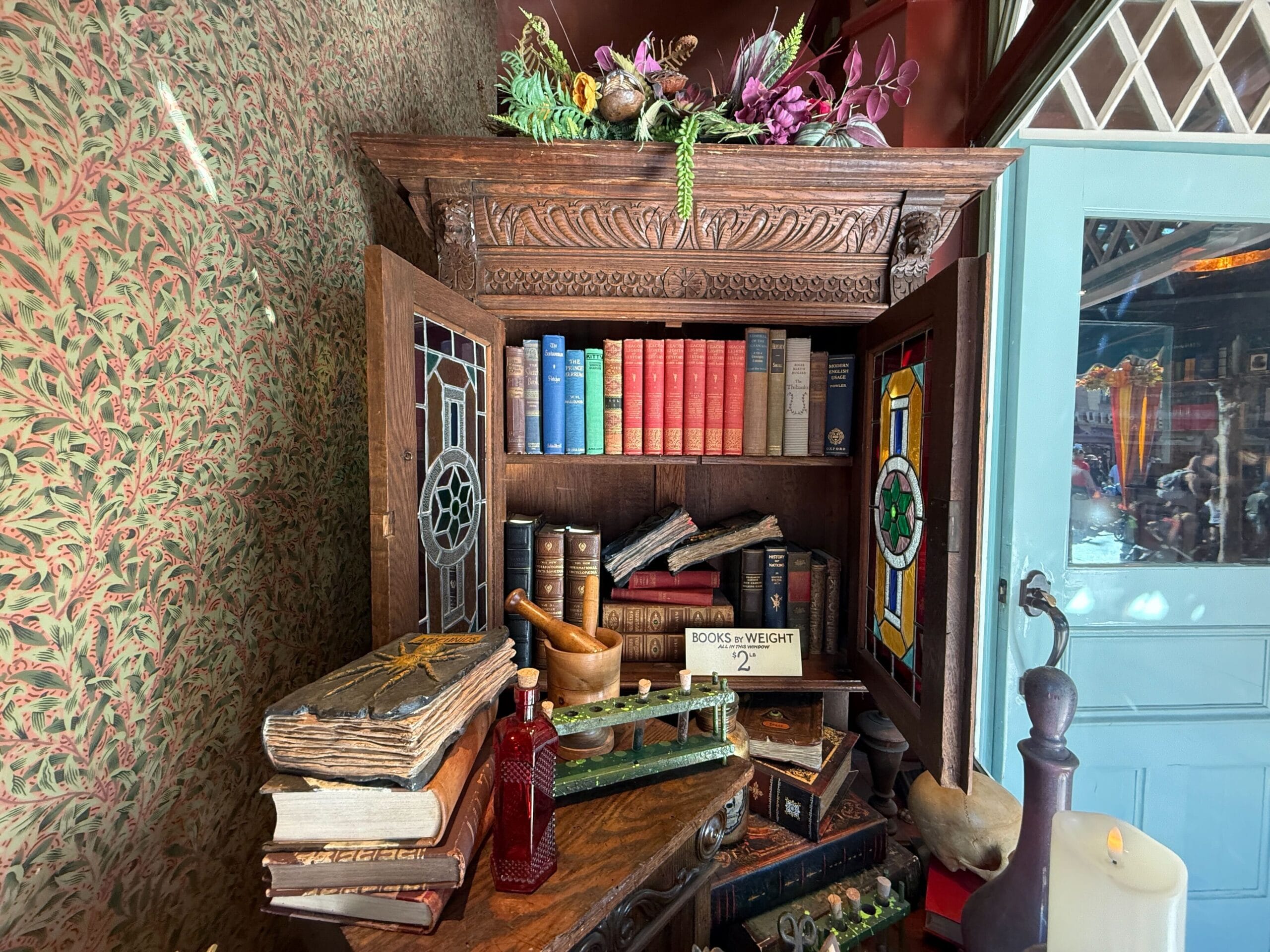 A wooden cabinet with open stained glass doors holding old books and vintage items, similar to antique decor in Disney park shops.
