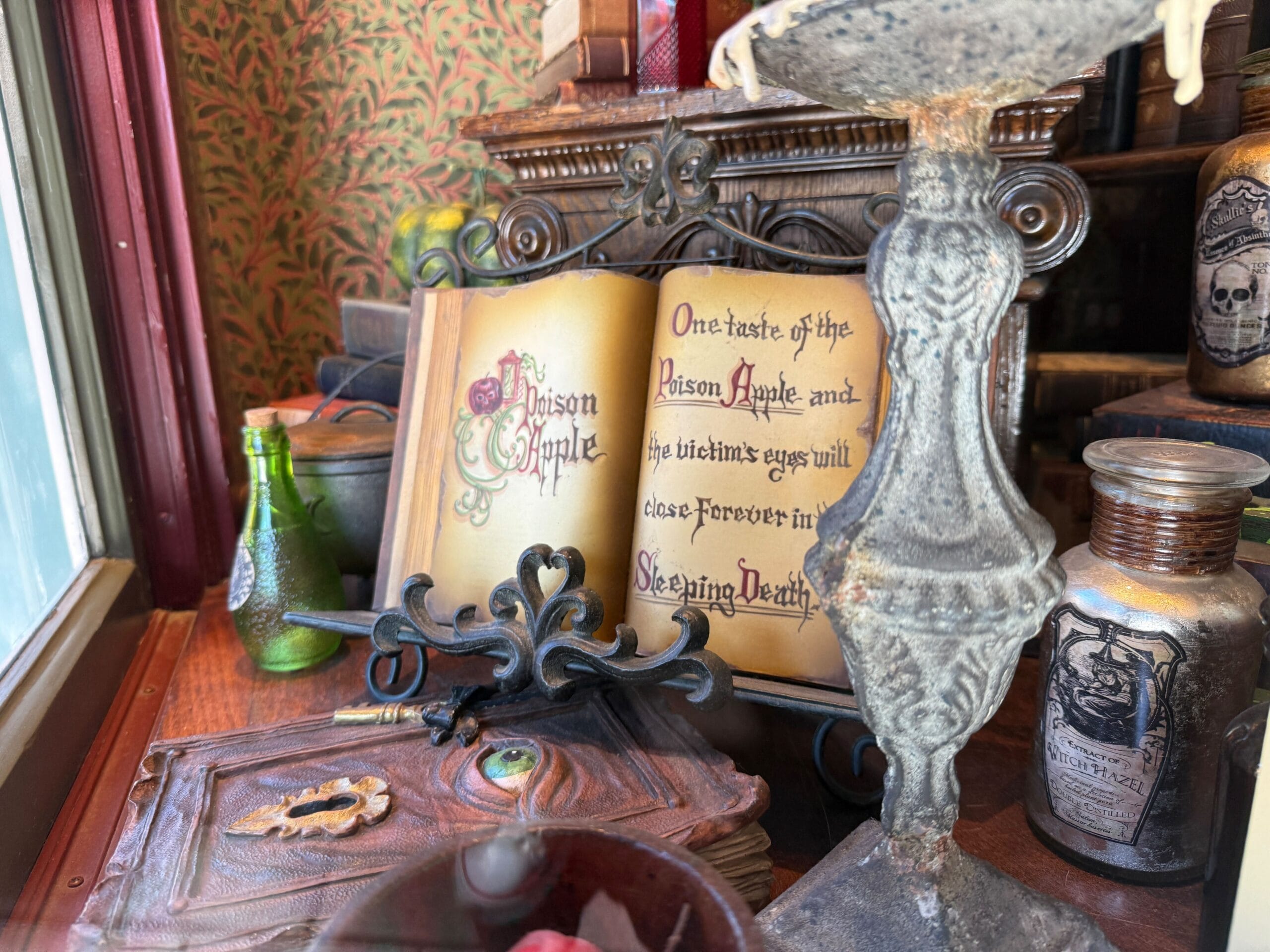 An old spellbook on display reads, "Poison Apple...the victim's eyes will close forever in the Sleeping Death," echoing Disney park magic.