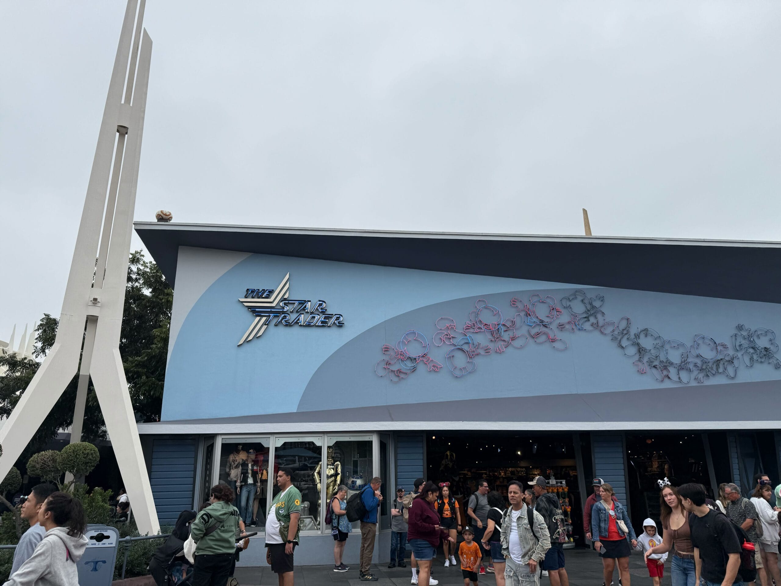 Guests gather outside Star Trader in Disneyland’s Tomorrowland under cloudy skies; no castle view, different from park icons.