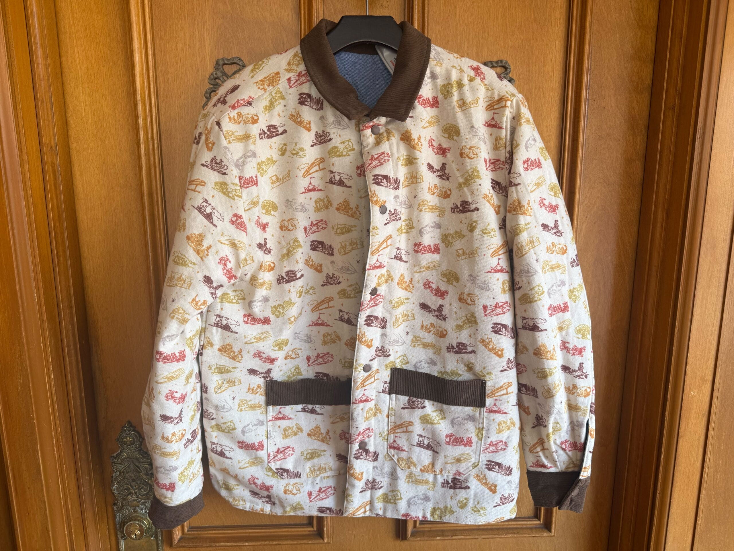 A patterned jacket with brown trim hangs on a wooden door, with vintage cars and text, evoking classic Disney park nostalgia.