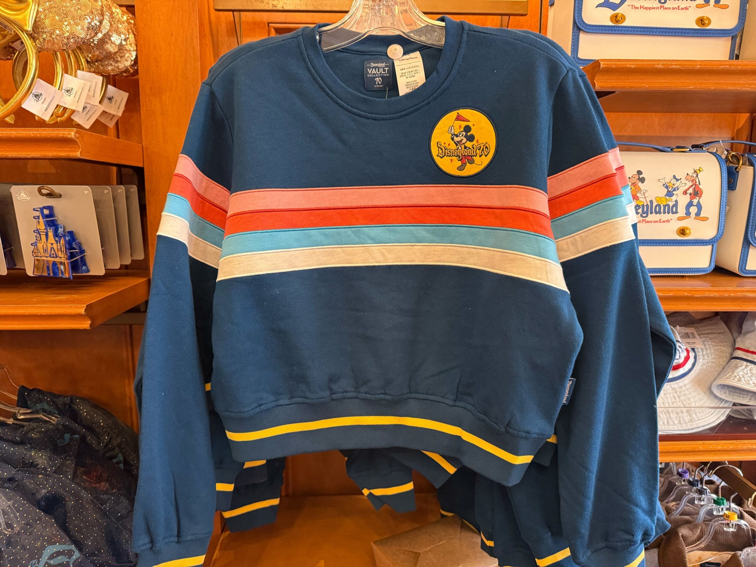 Navy sweatshirt with colorful stripes and a Disneyland 1955 patch, seen on a store rack in the park’s Main Street shop.