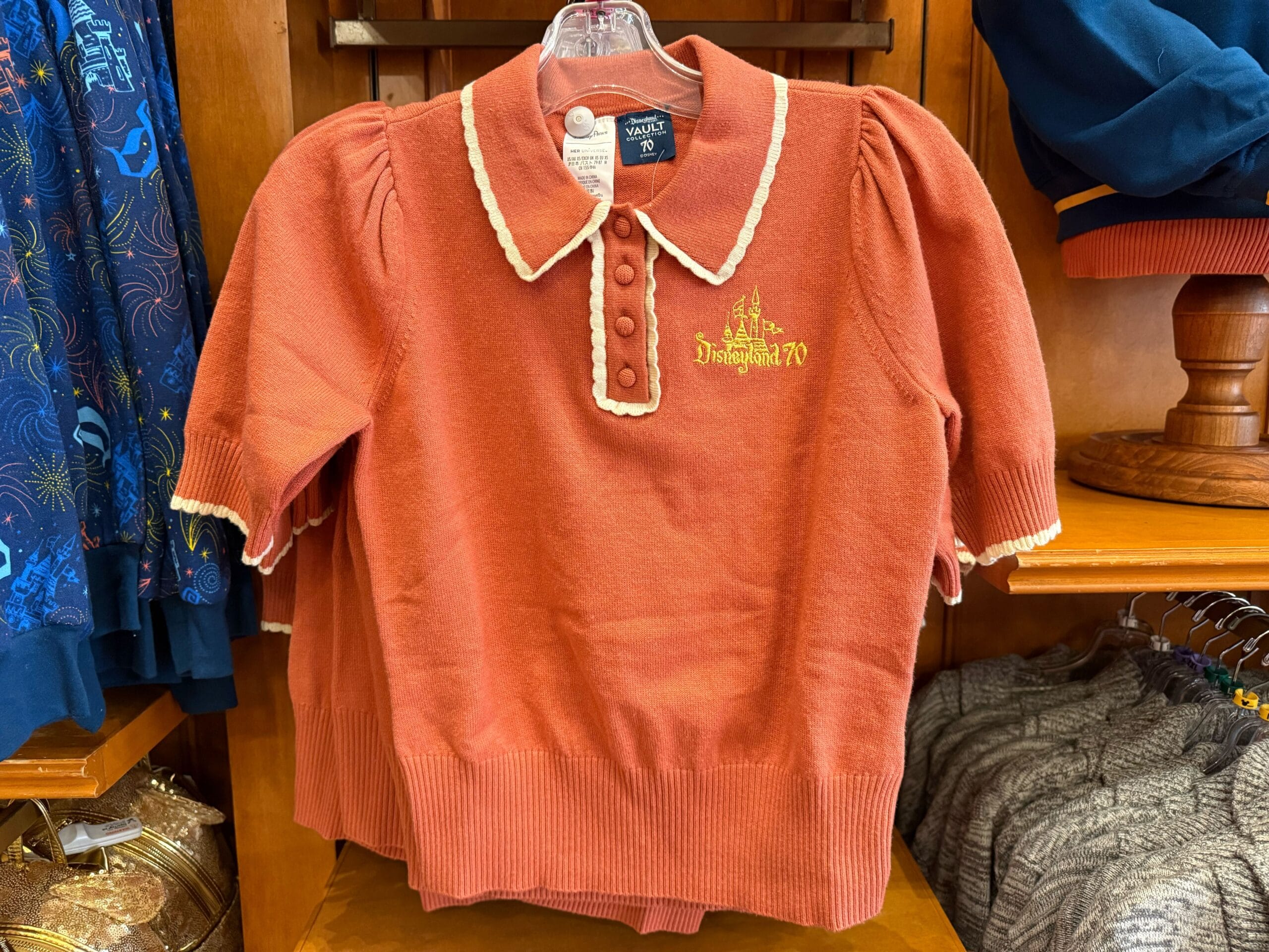 Rust short-sleeve sweater with collar, buttons, and "Disneyland 70" in gold on the chest, celebrating Disneyland’s legacy.