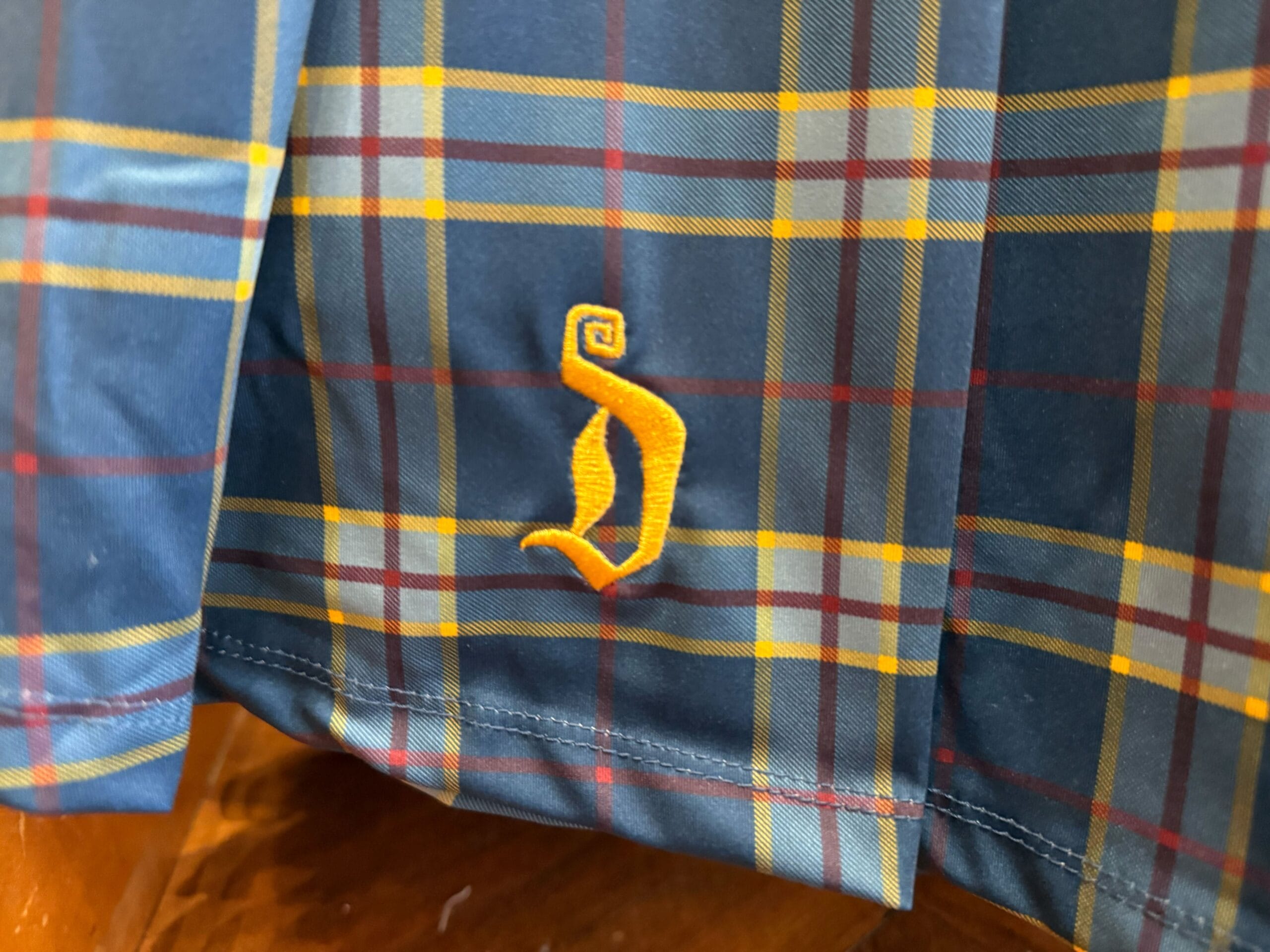 Blue plaid fabric with yellow and red lines, topped by a gold spiral "J" reminiscent of whimsical Disney park monogram designs.